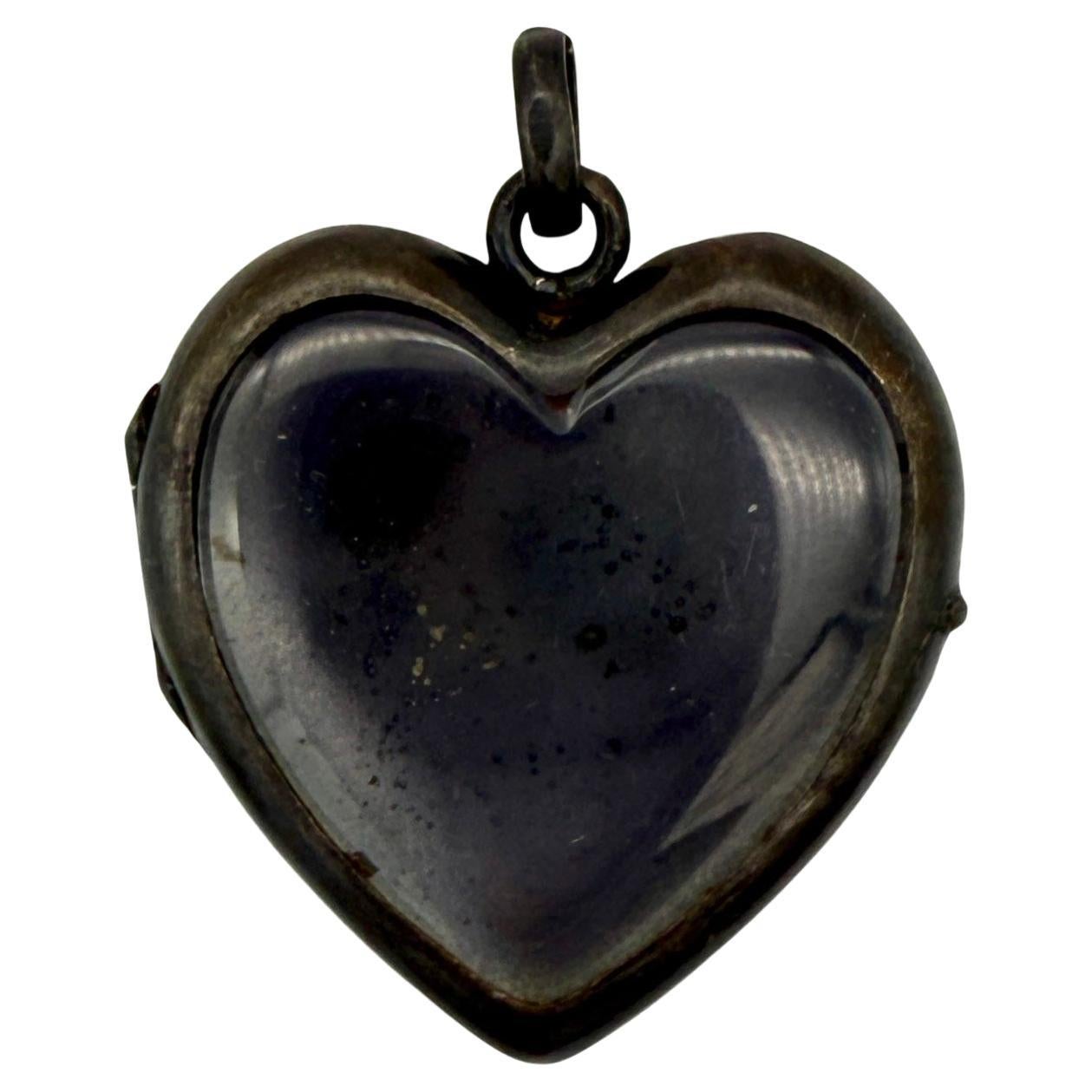 This fine size locket heart pendant was created in the last two decades of the 19th century. The heart is a locket pendant with a glass back. The front of the heart locket is made out of one piece of gunmetal. The hinged back of the locket consists