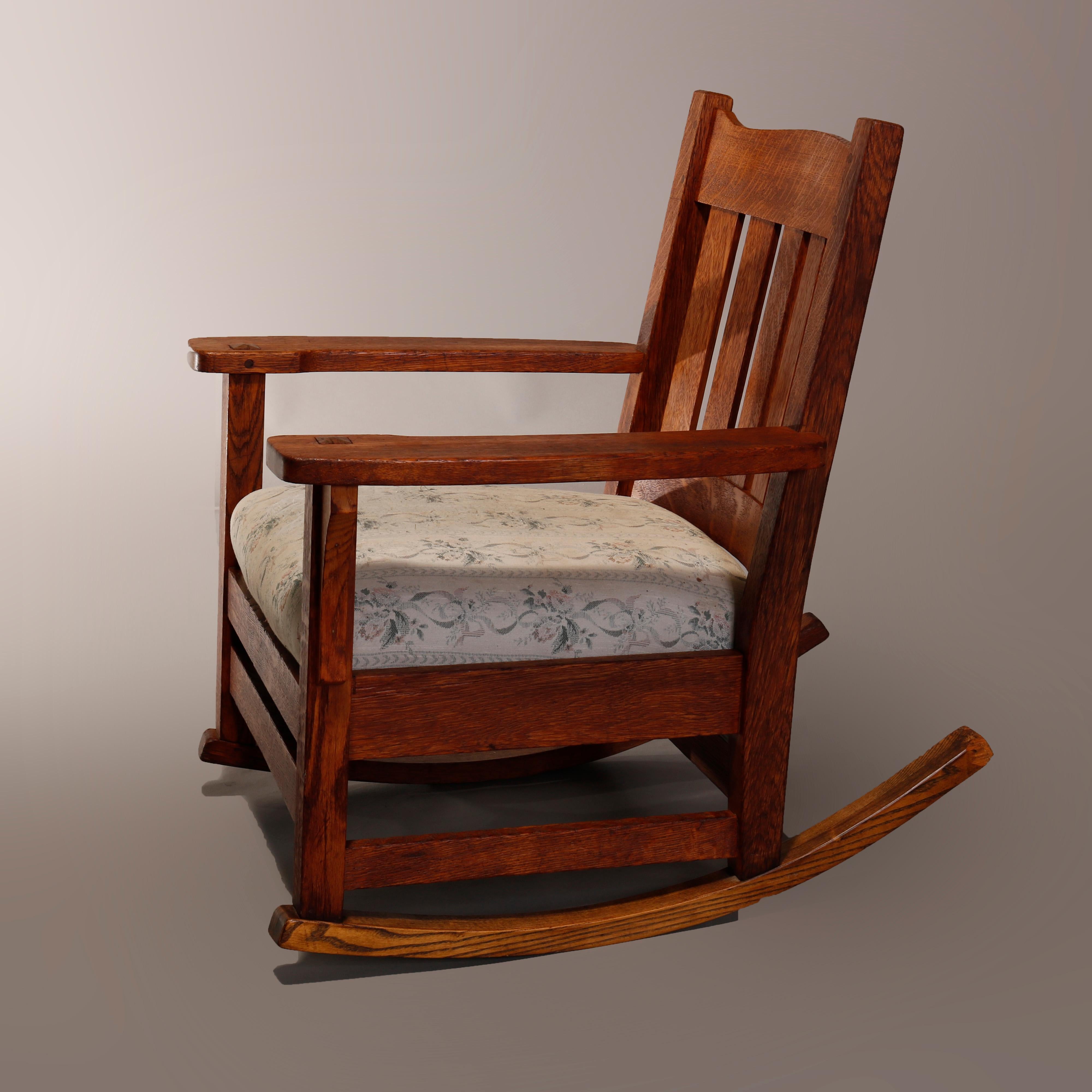 An antique Arts & Crafts Mission rocker in the manner of Stickley offers oak construction with shaped rail over slat back and cushioned seat, circa 1910.

Measures: 32.25