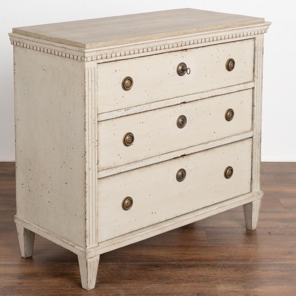 Lovely gustavian pine chest of three drawers with fluted columns, dentil molding and tapered fluted feet.
The newer, professionally applied layered gray painted finish has undertones of white and is gently distressed to fit the age of the chest.
