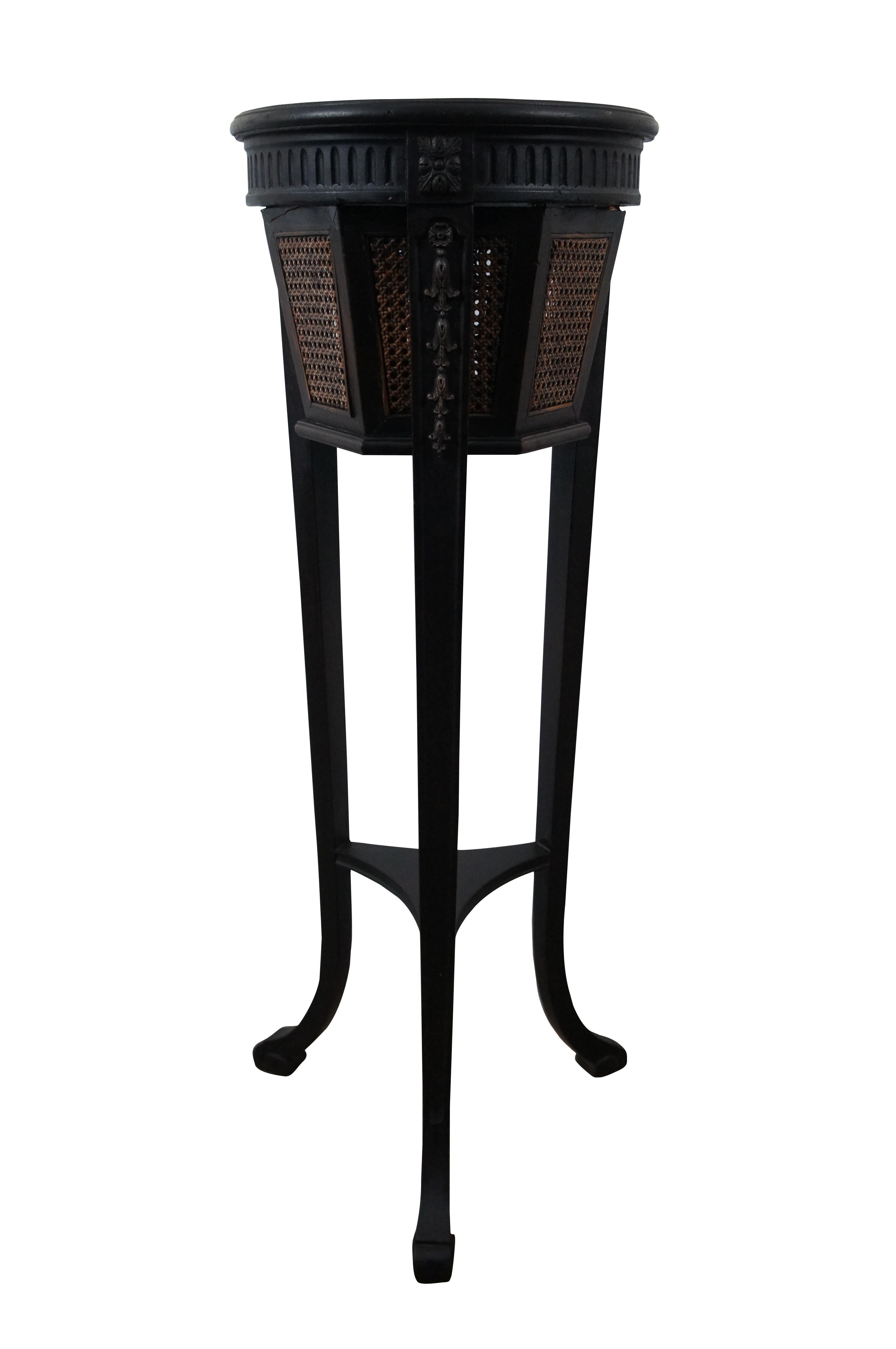 Antique Gustavian style plant stand featuring black painted mahogany frame with hexagon shaped caned planter, tapered tripod legs, and fluted and carved floral accents.


DIMENSIONS

13” x 36” (Diameter x Height)