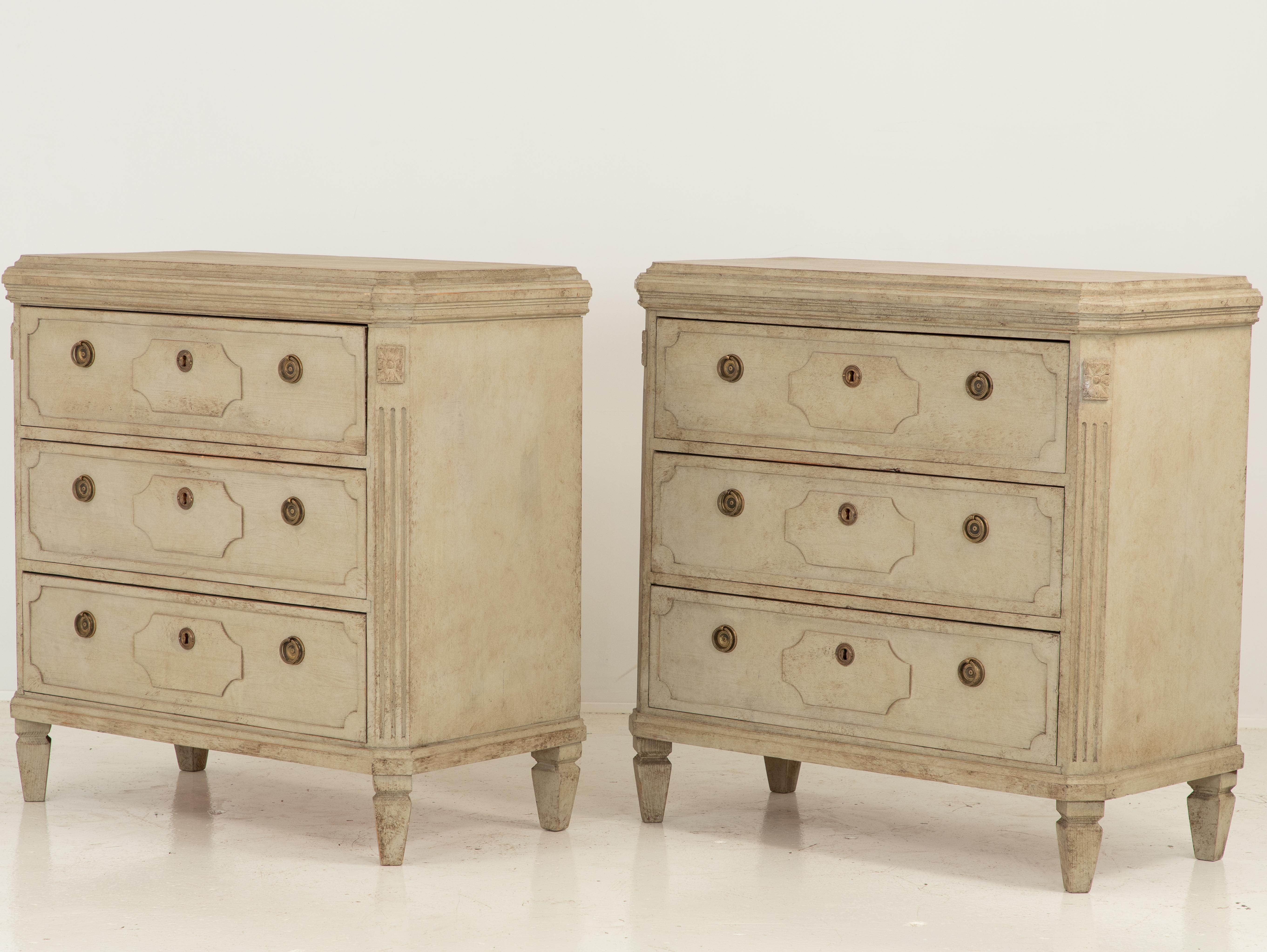 An early 20th century pair of Swedish Gustavian style chests of drawers. Each commode has three drawers with brass ring pulls and escutcheons. Each drawer has beautifully carved lozenges. Canted corner with medallions and reeded detail on the