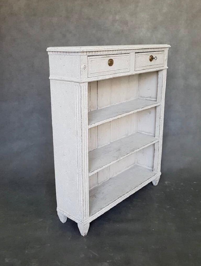Small open bookcase with two-drawers and three-shelves in the Gustavian style. This piece is in grey and white color. It was produced in Sweden, circa 1860.
   