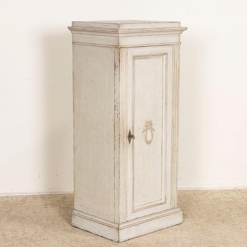 Narrow cabinets are difficult to find, making this lovely gustavian style pedestal cupboard a special find. Take note of the lovely (later applied) soft gray layered painted finish which adds a touch of grace to this romantic piece. At only 21.5