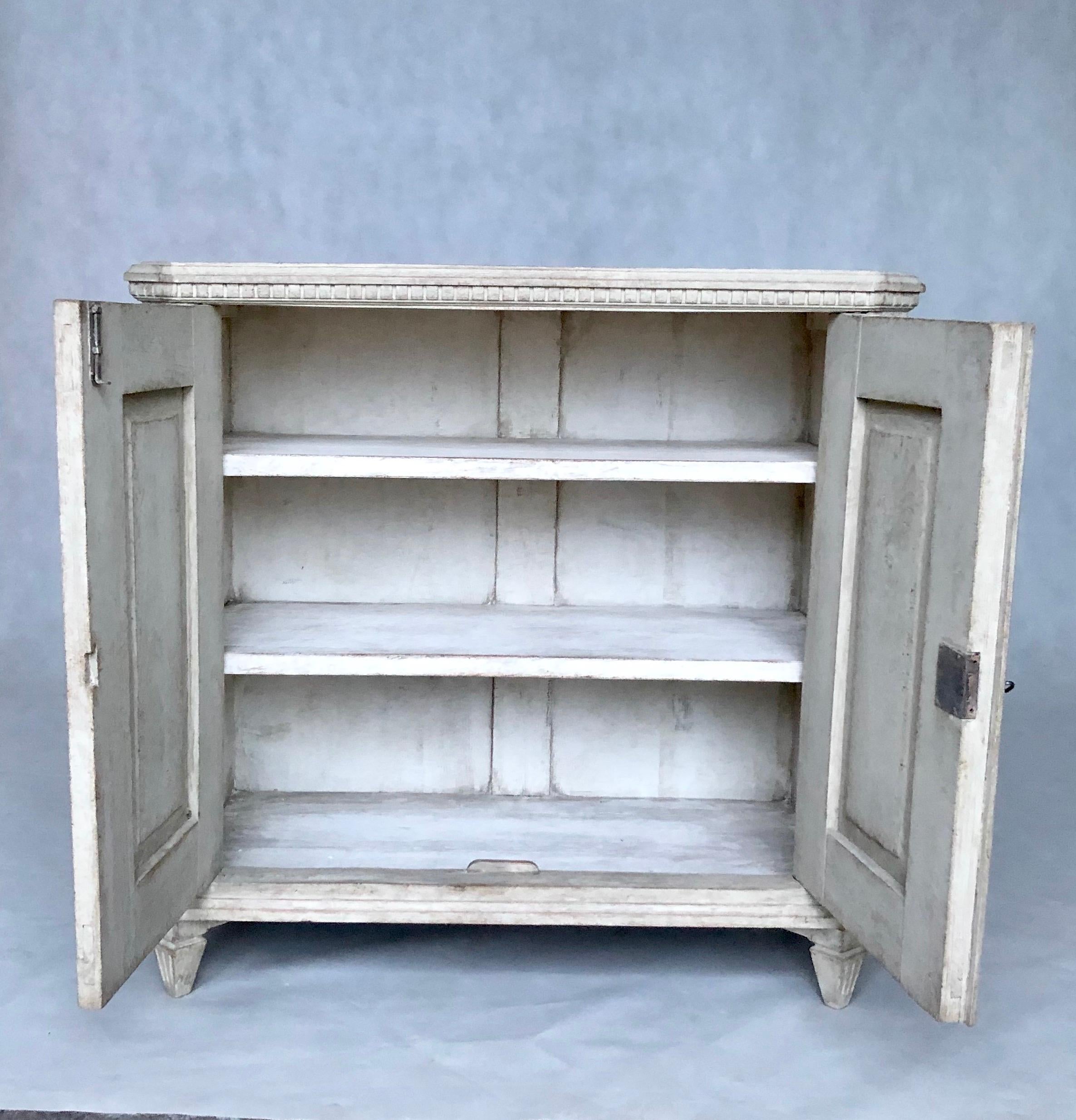 This is a beautiful Gustavian style sideboard features two doors and is colored antique white. The front has delicate decorations, while the corners are cut. Under the top are teeth.