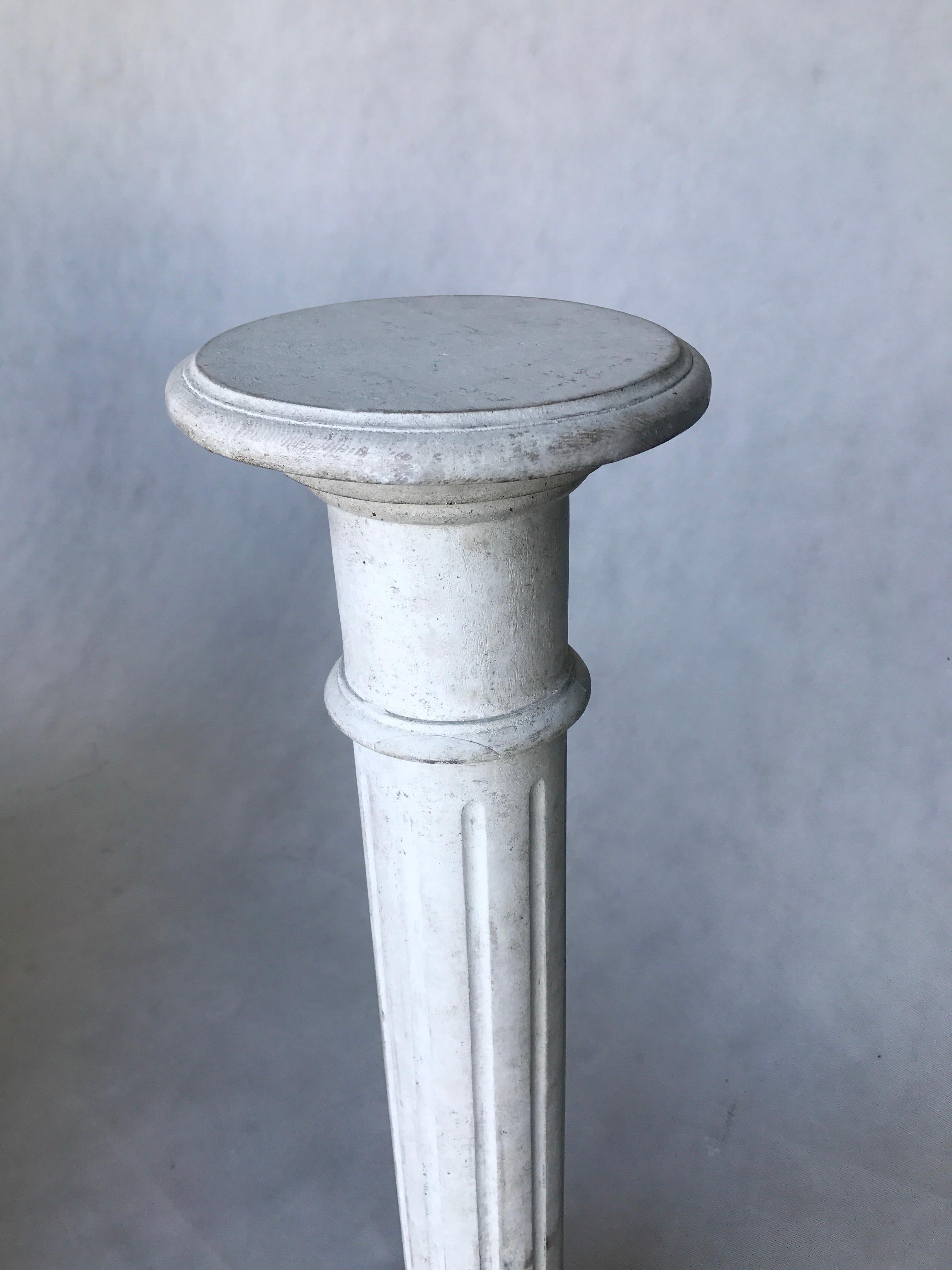 This slender column from the Gustavian Style is made of white-lacquered wood. The piece features vertical ornamental indents, a square base, and a rounded top.