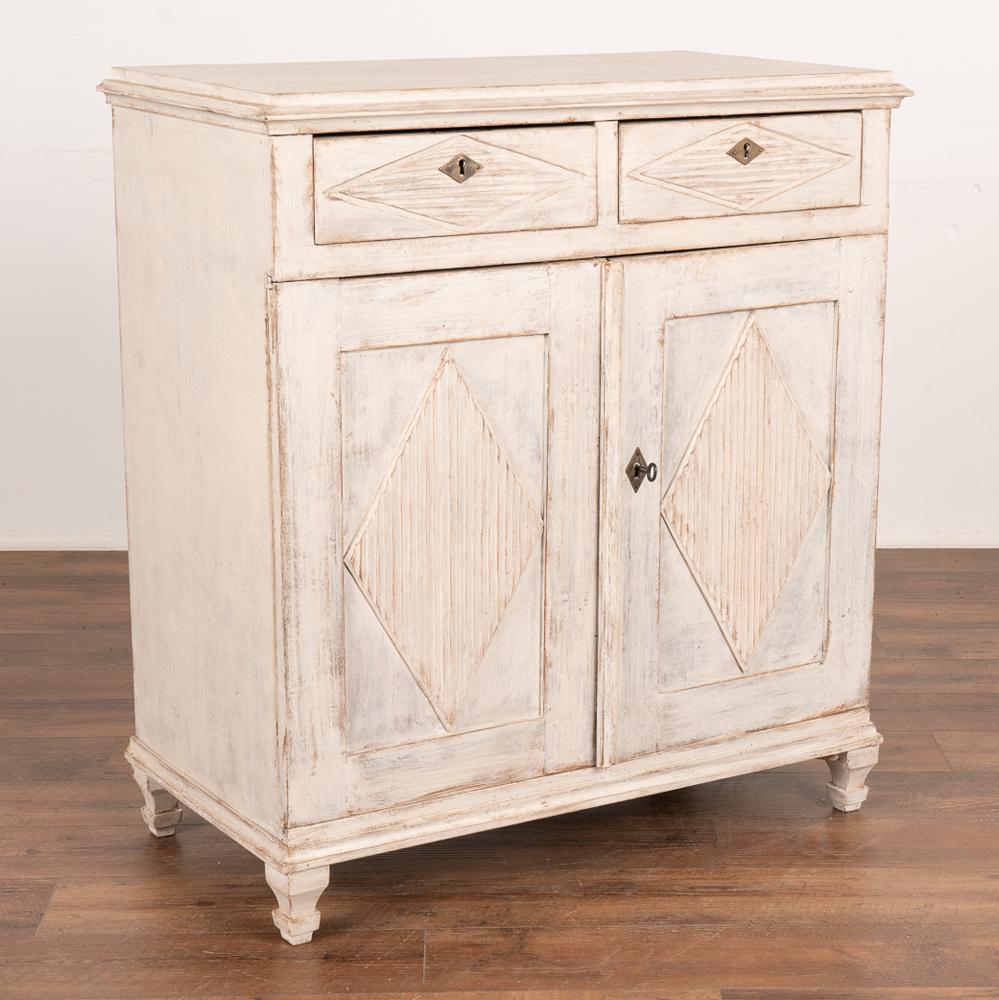 Gustavian white painted pine sideboard or server cabinet with three interior shelves.
Traditional decorative fluted diamond panels, raised on carved feet.
The newer, professionally applied white painted finish is lightly distressed to fit the age