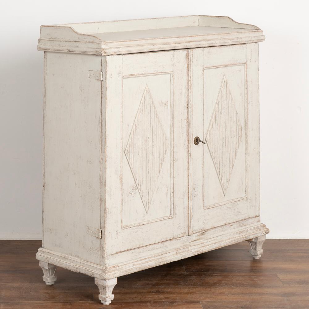 Gustavian white painted tall pine sideboard or server cabinet.
Traditional decorative fluted diamond panels, tapered fluted feet.
Interior hook and latch hold left door in place when closed. One key included for right door. 
Interior holds three