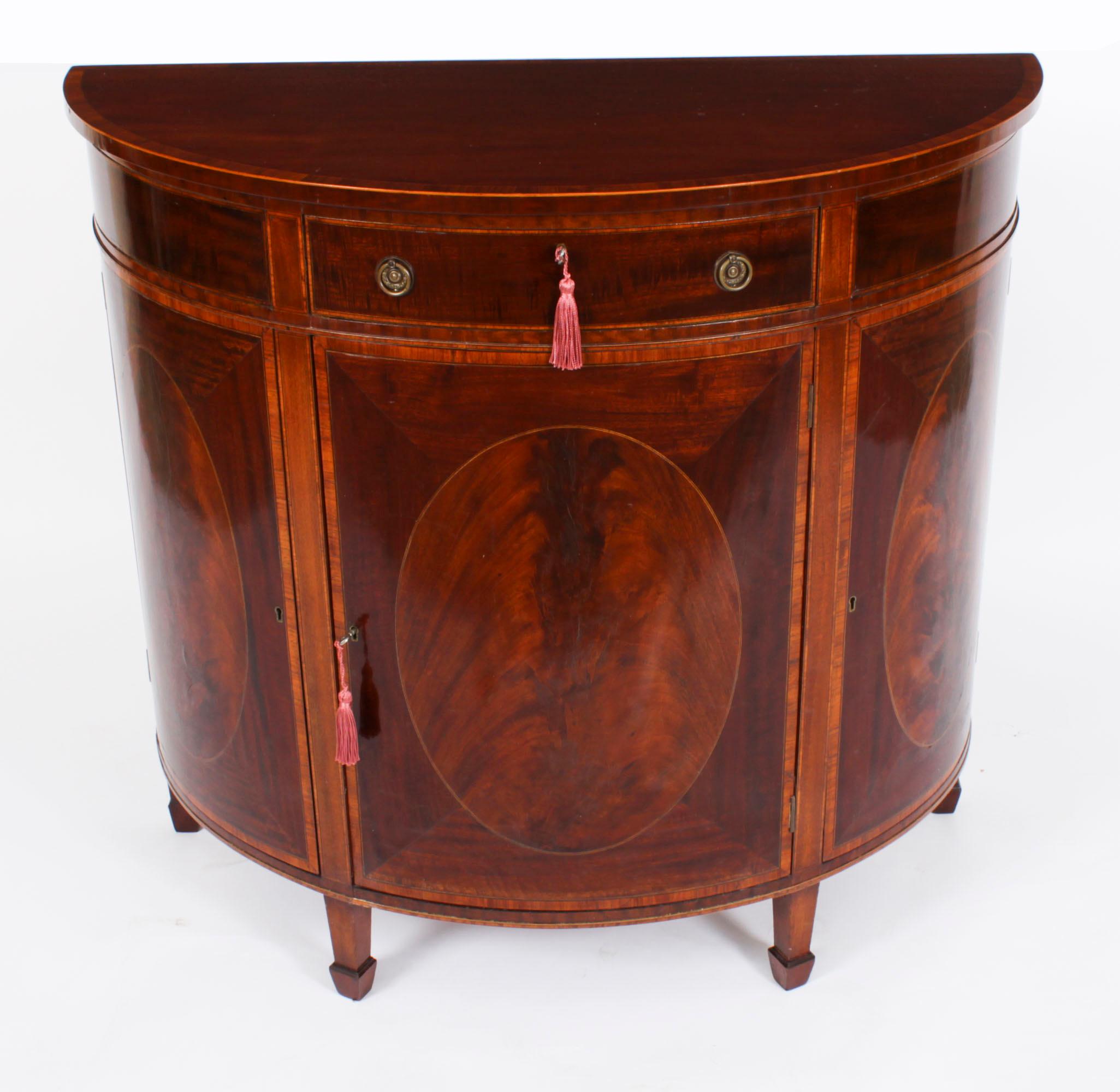 This is a superb antique George III Revival demilune flame mahogany bowfront side cabinet, circa 1880 in date.

The half moon top is beautifully crossbanded in satin wood above a capacious central drawer in the frieze. There are three cupboard doors