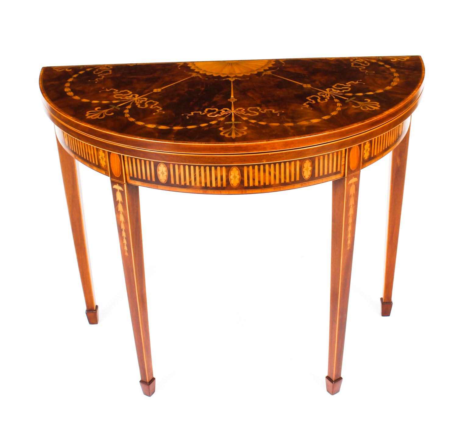 A superb Sheraton Revival flame mahogany half round fold over card table, circa 1870 in date.

The top with cross banding and stunning marquetry decoration of shell, ribbons and swags over a decorative frieze inlaid with shells and satinwood