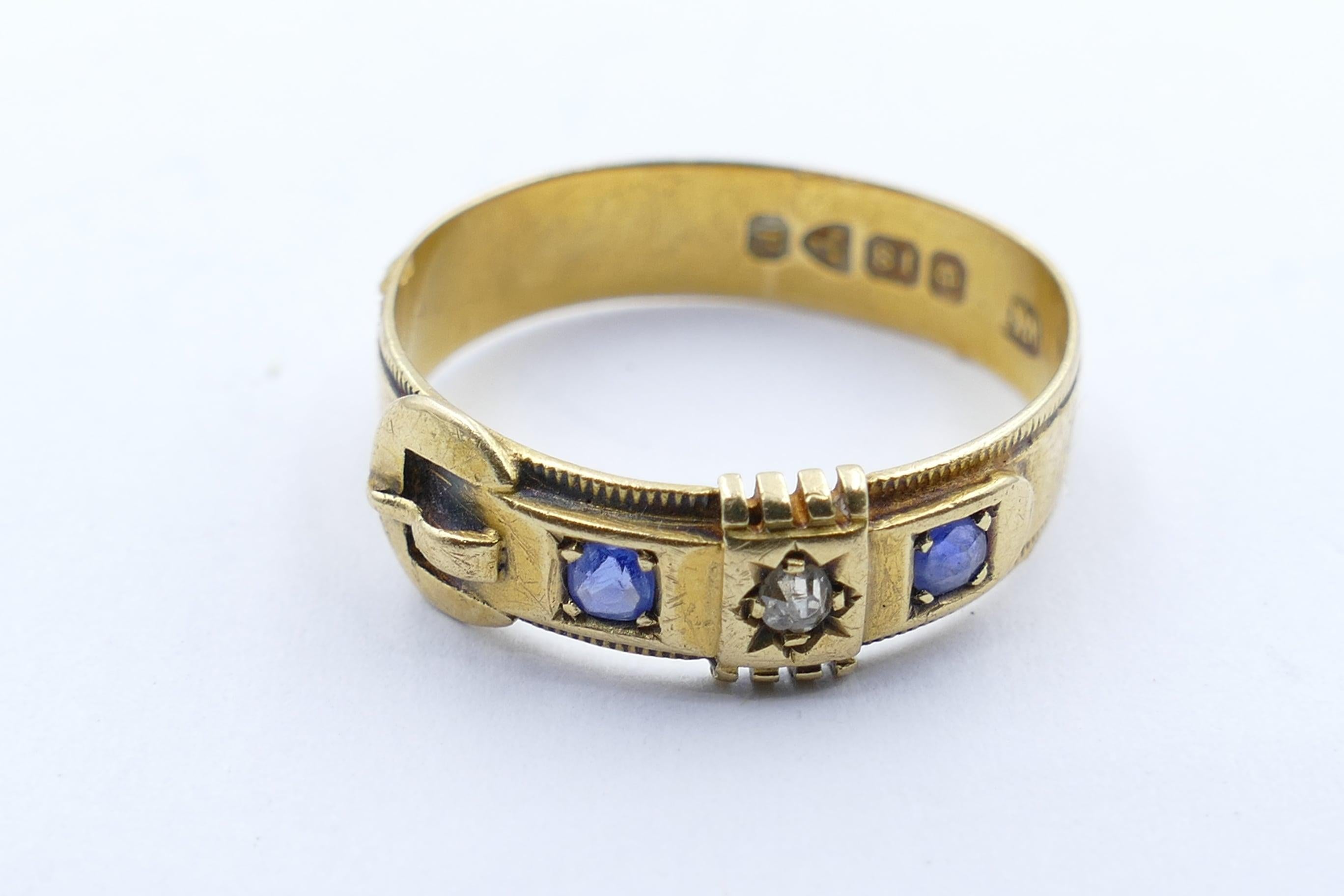 This beautifully preserved Antique (Victorian) Buckle Ring is set with a Diamond as the centrepiece and is flanked by 2 lovely old Ceylon Sapphires, round cut & bead set. The Diamond is old European cut.
The Ring features hallmarks pertaining to