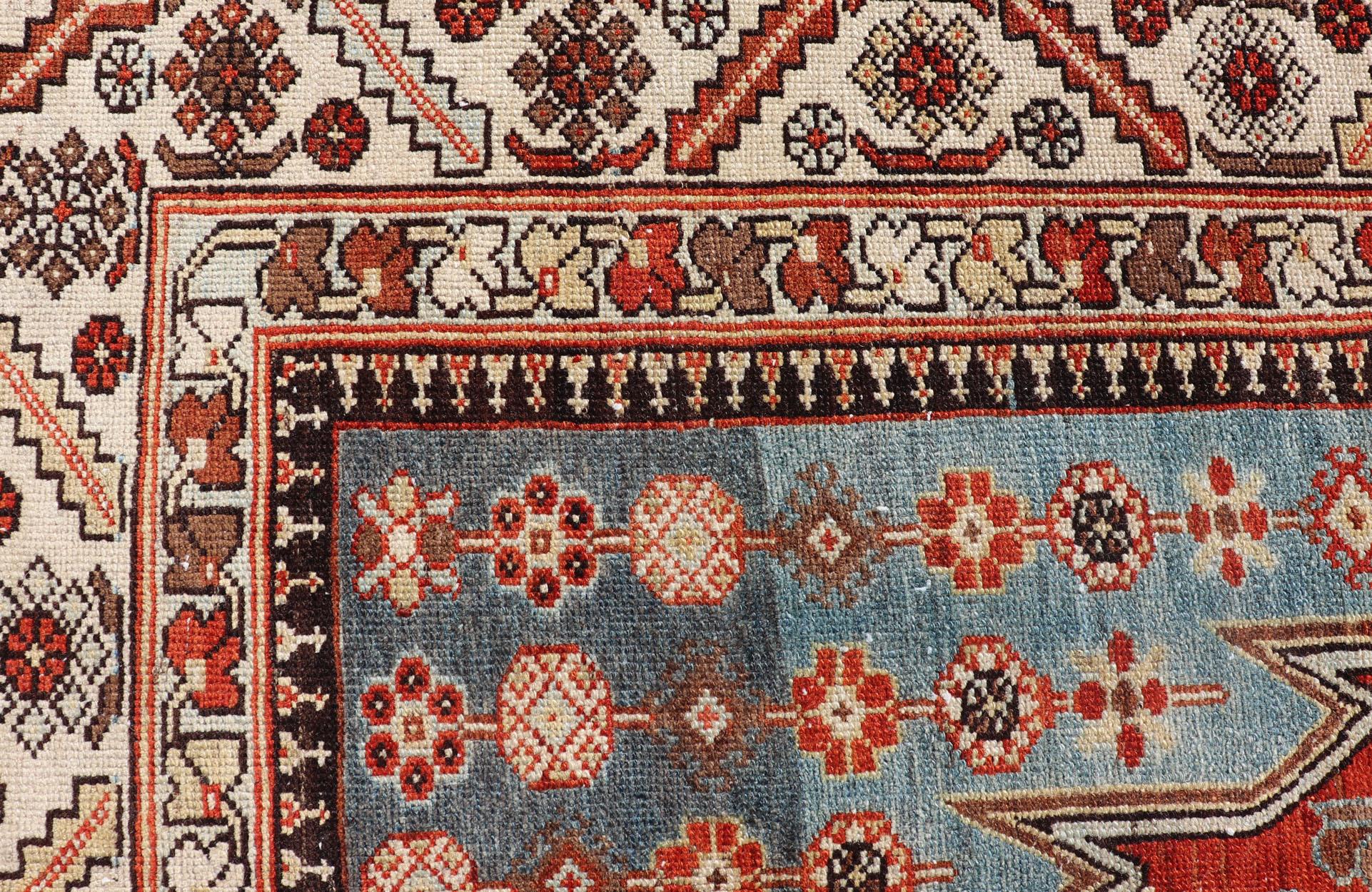 This unique Persian Hamadan Gallery rug features an exquisite design composed of a vertical arrangement of red and brown geometric medallions surrounded by a variety of intricate motifs. The rug is set upon a Dark and Light Blue background, and is