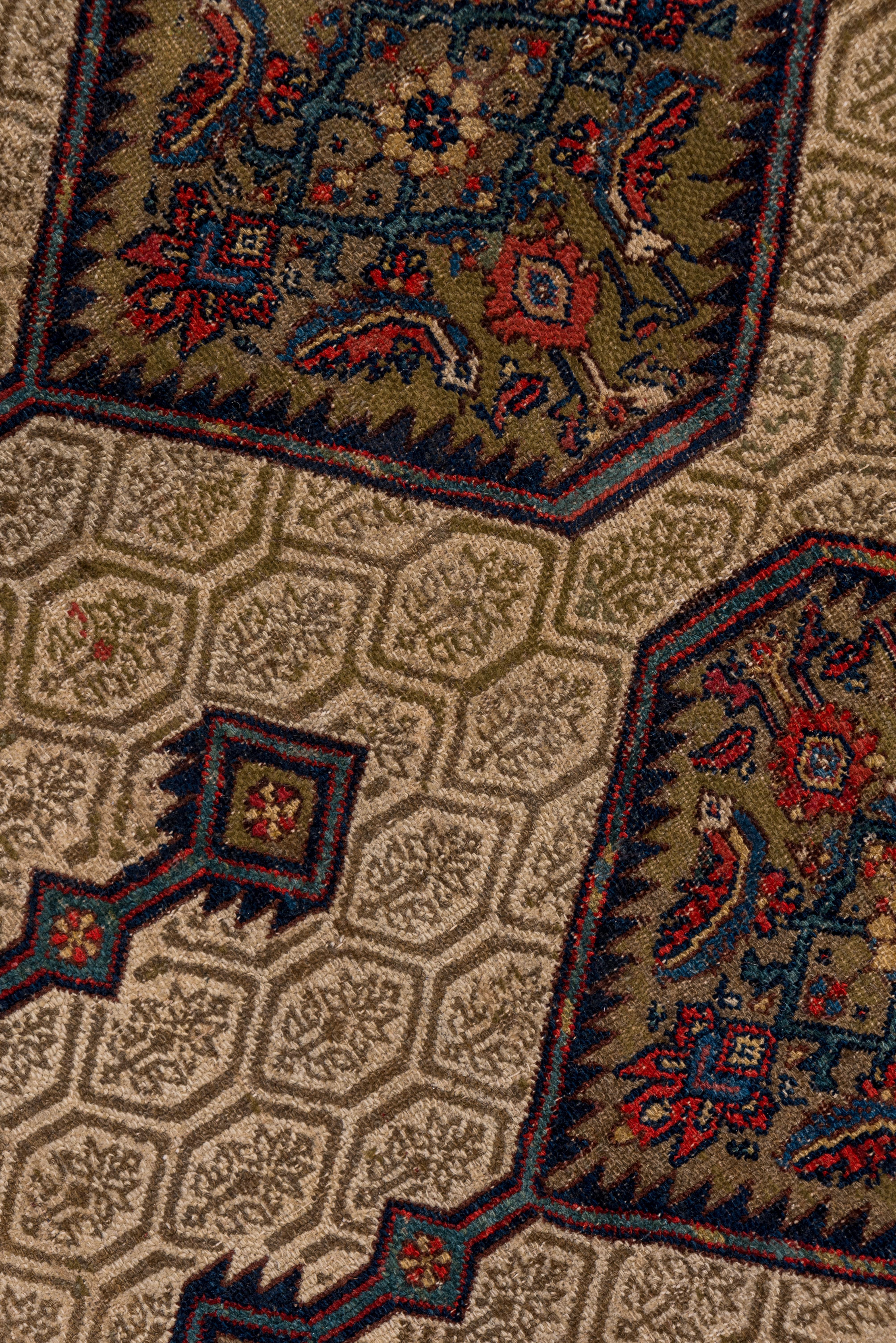 Within a broad, plain camel-tone border, this west Persian village carpet presents a cream field with a small hexagon and flower all-over pattern underlying full and partial large medallions with internal Herati patterns accented in green, dark