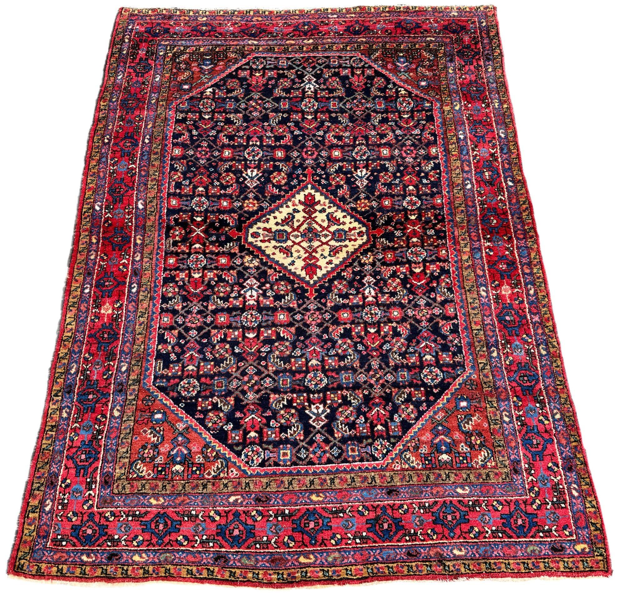 Magnifique tapis ancien de Hamadan, tissé vers 1920. Le tapis présente un petit médaillon ivoire sur un champ Herati indigo profond entouré d'une riche bordure rouge. Tissé avec de la laine douce et veloutée et des couleurs secondaires