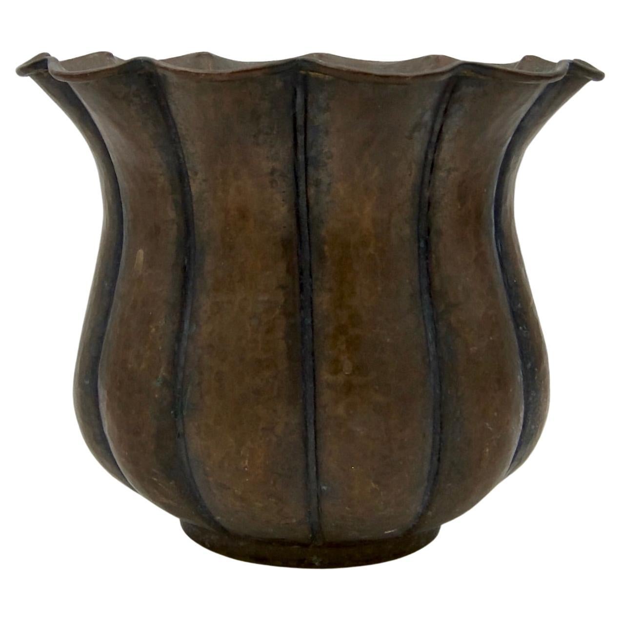 An antique hammered copper planter or cachepot in the Arts and Crafts style. The planter dates to the early 20th century and was hand-raised showing Hammer marks overall. The fluted body rests on a circular foot; the body swells outward before
