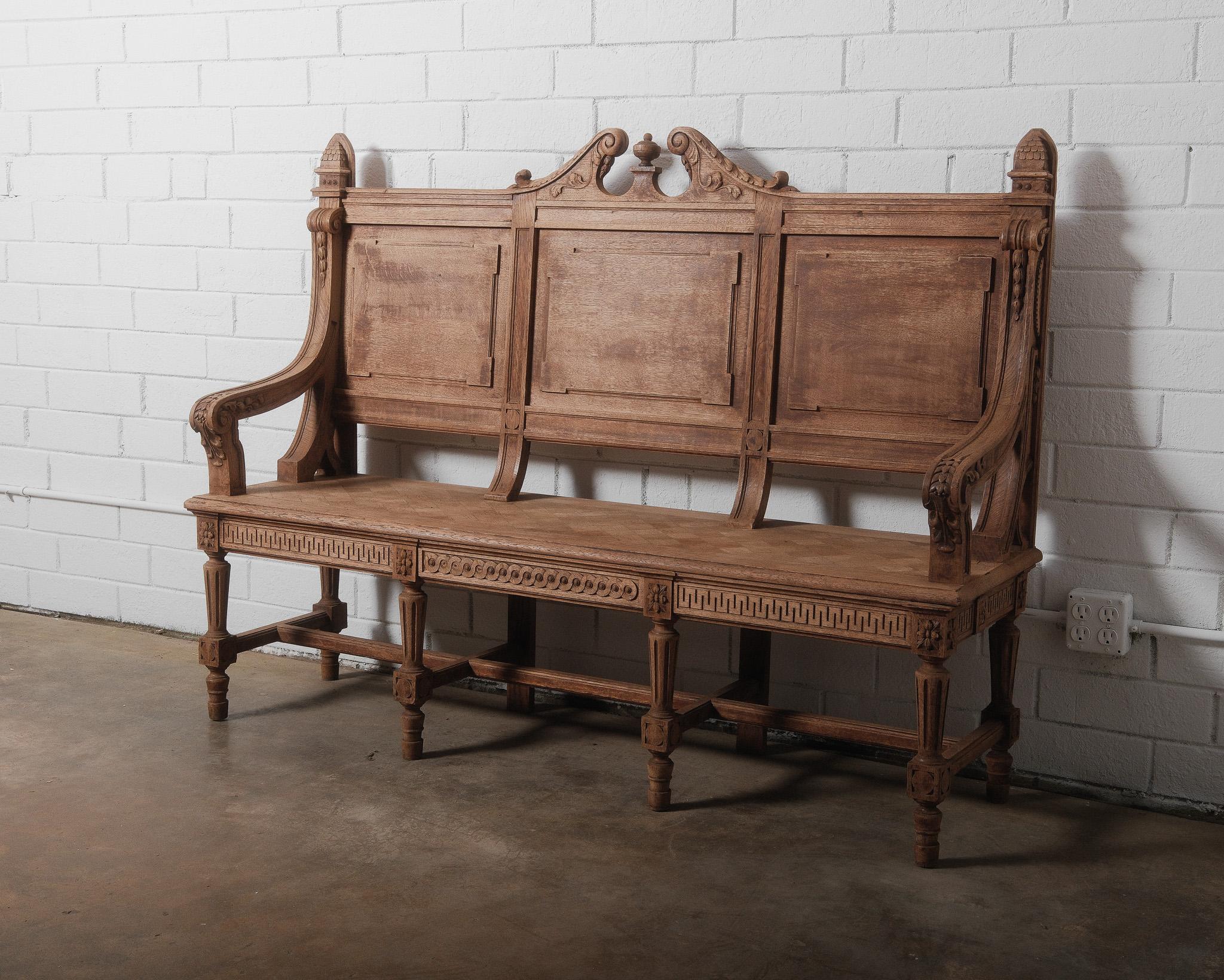 This exquisite antique French bench showcases the opulence of Renaissance Revival craftsmanship, featuring intricate hand-carved detailing throughout. The high back is adorned with ornate scrolling motifs, classical paneling, and a central finial,