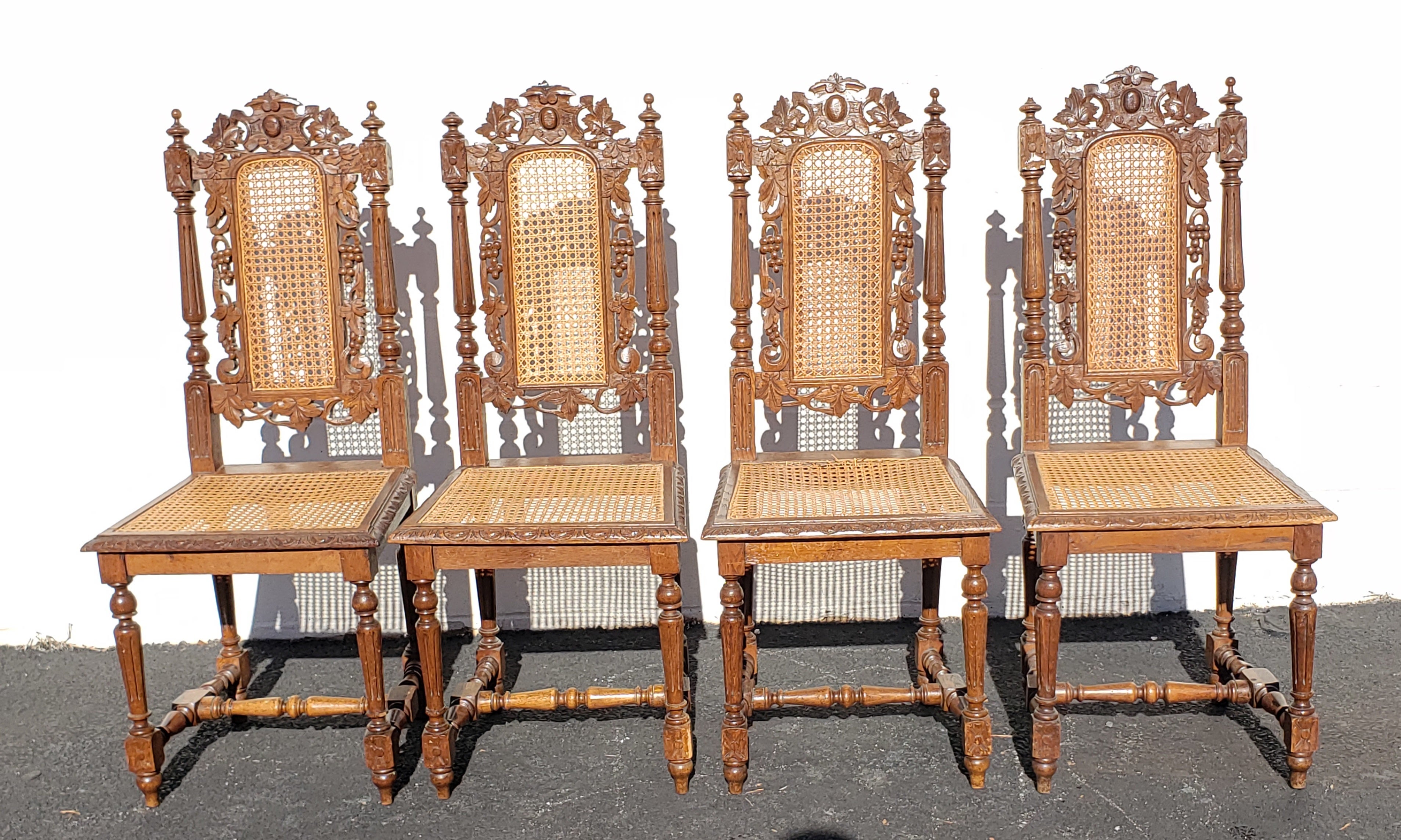 A very decorative, intricately carved antique Jacobean chairs in oak and cane. A set of 4. They have elaborately carved backs with carved and pierced central panels and a carved back rail depicting vine leaves. The side supports are elaborately