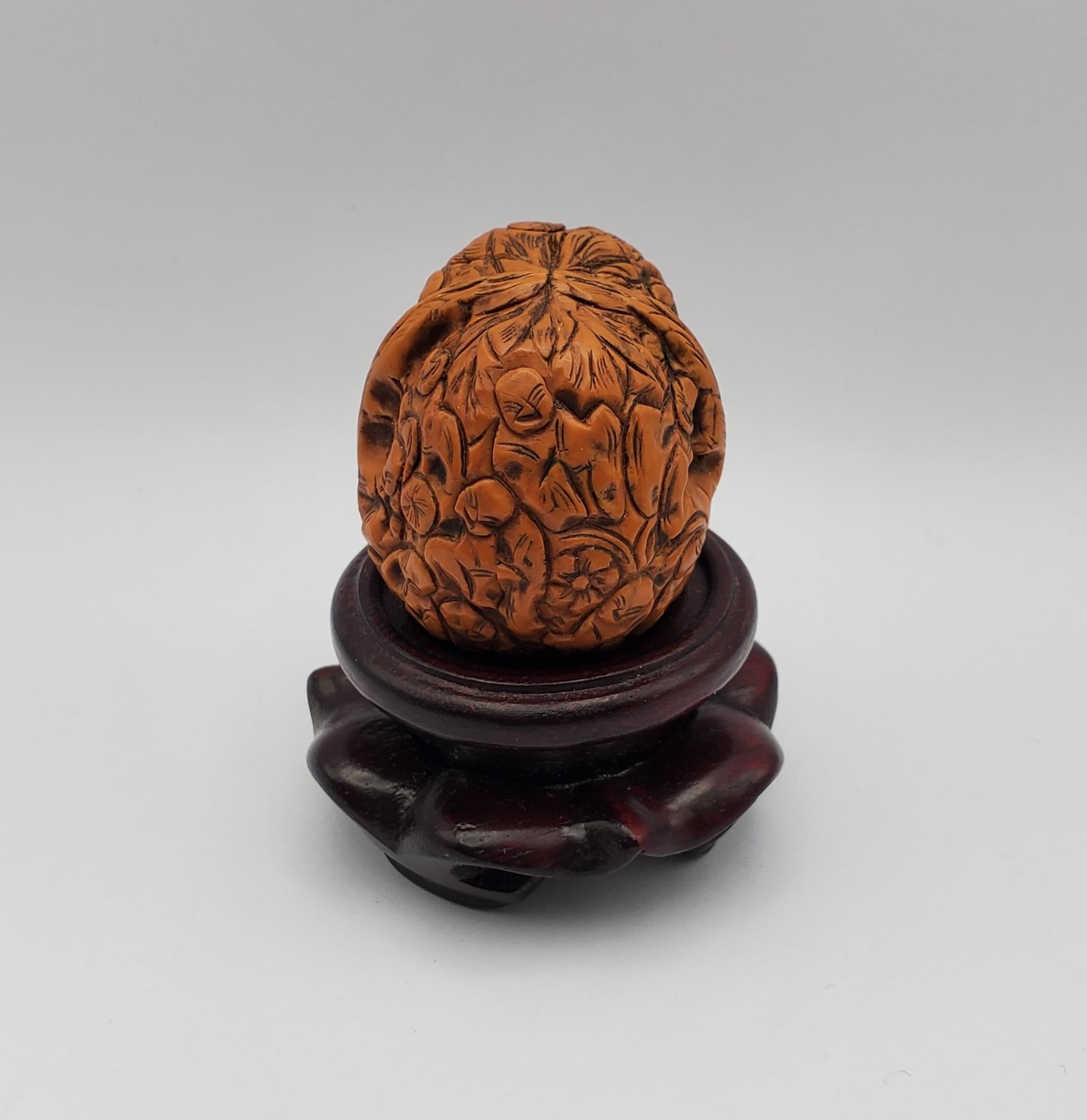 Beautiful hand carved Netsuke walnut sculpture depicting the 1000 faces motif with a carved wooden pedestal stand. The faces carved into the delicate shell represent Buddhist monks. There are some natural indentions in the walnut exterior but no