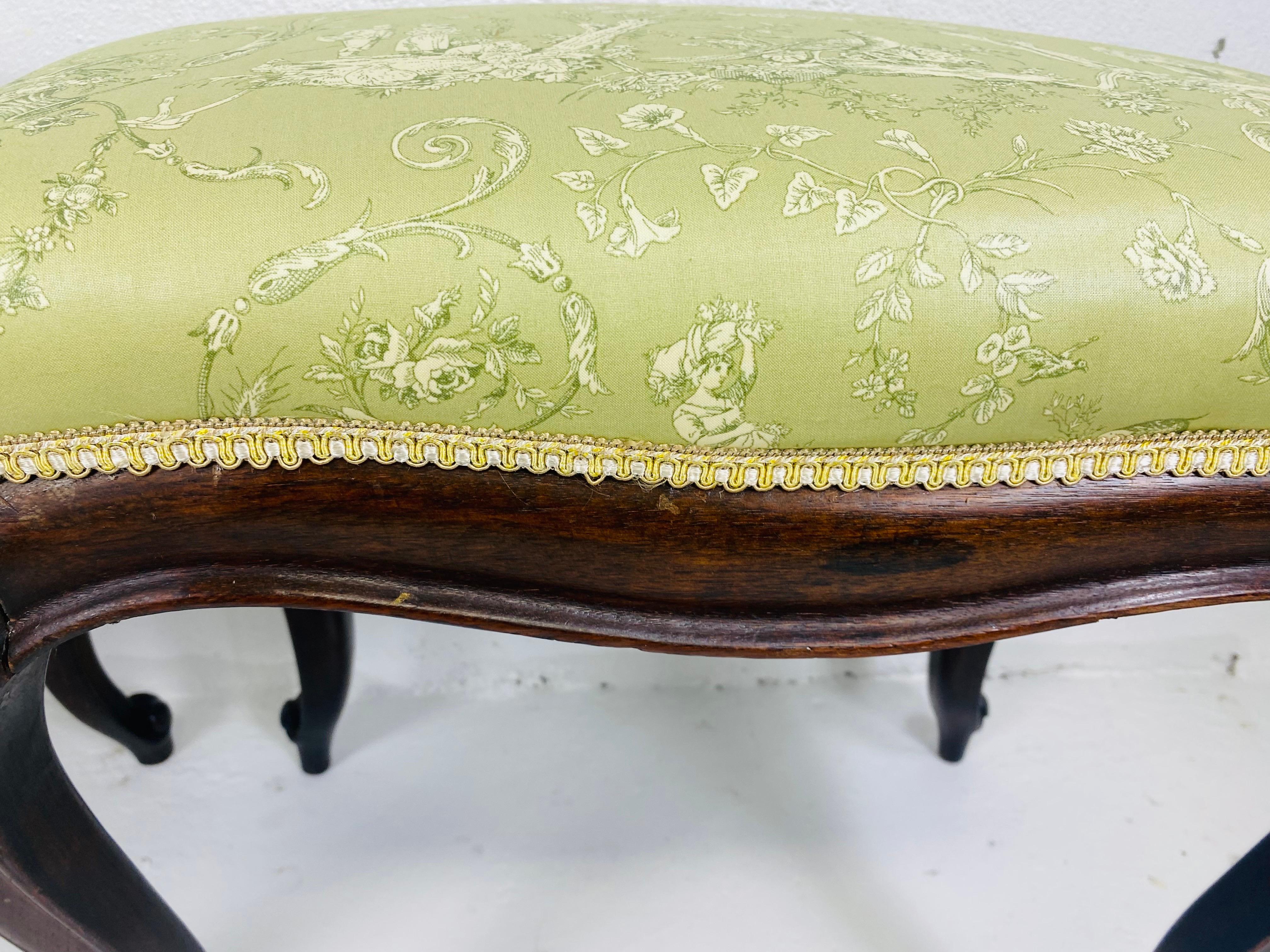 This is a pair of early 20th century handcarved walnut French country style benches. These benches have been newly upholstered in a sage green French country Toile. The benches have a soft curved leg with hand carved details at the base and around