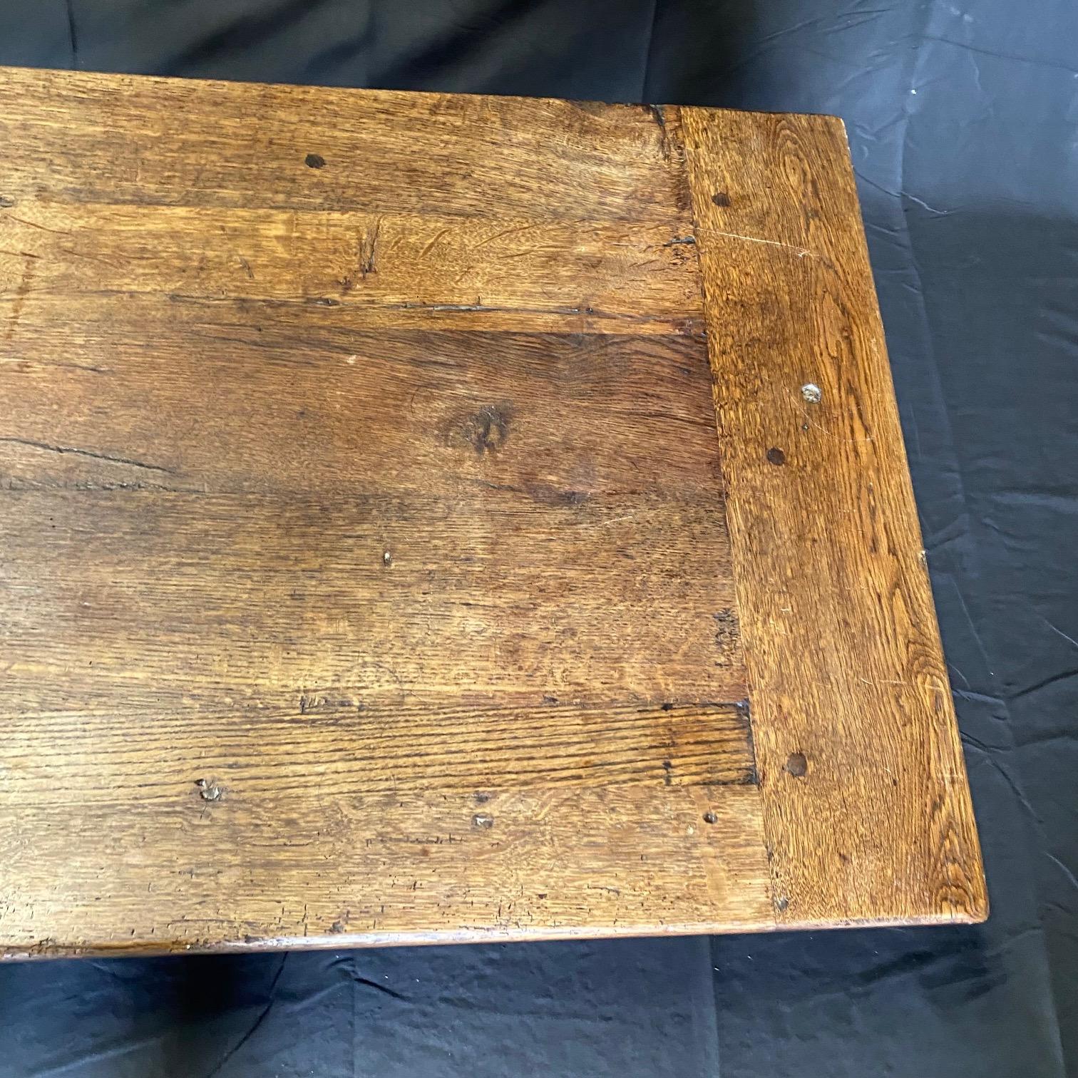 Antique French oak coffee table is a rich brown with gorgeous natural graining running along the plank top with breadboard ends. The legs are hand turned and connected with an H stretcher, and there are two spacious beautifully dovetailed drawers in