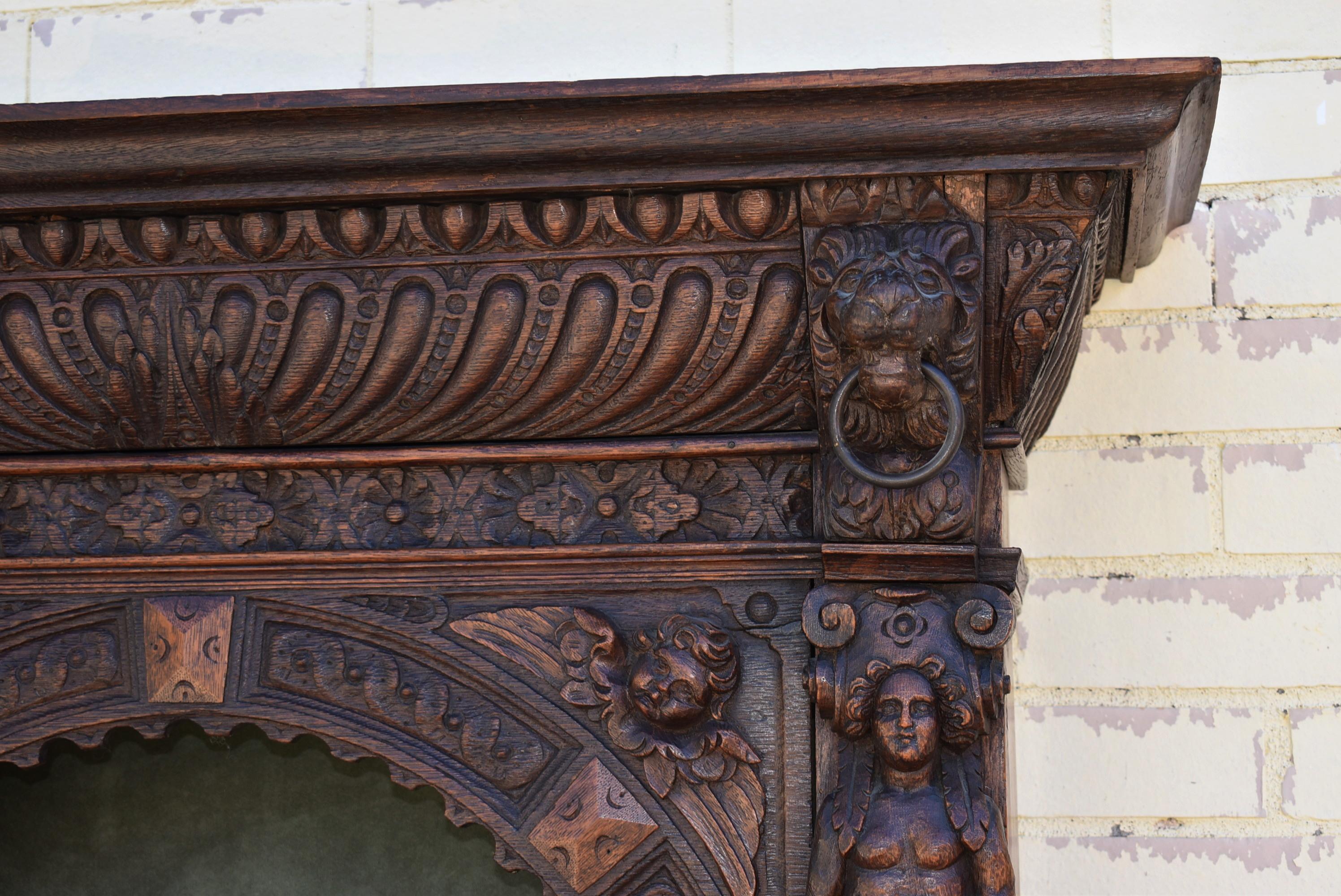 Antique hand carved oak Gothic Revival English wall cabinet, circa 1890s. Lion head with iron rings through the mouths. Removable shelves. Carved winged cherubs. 47