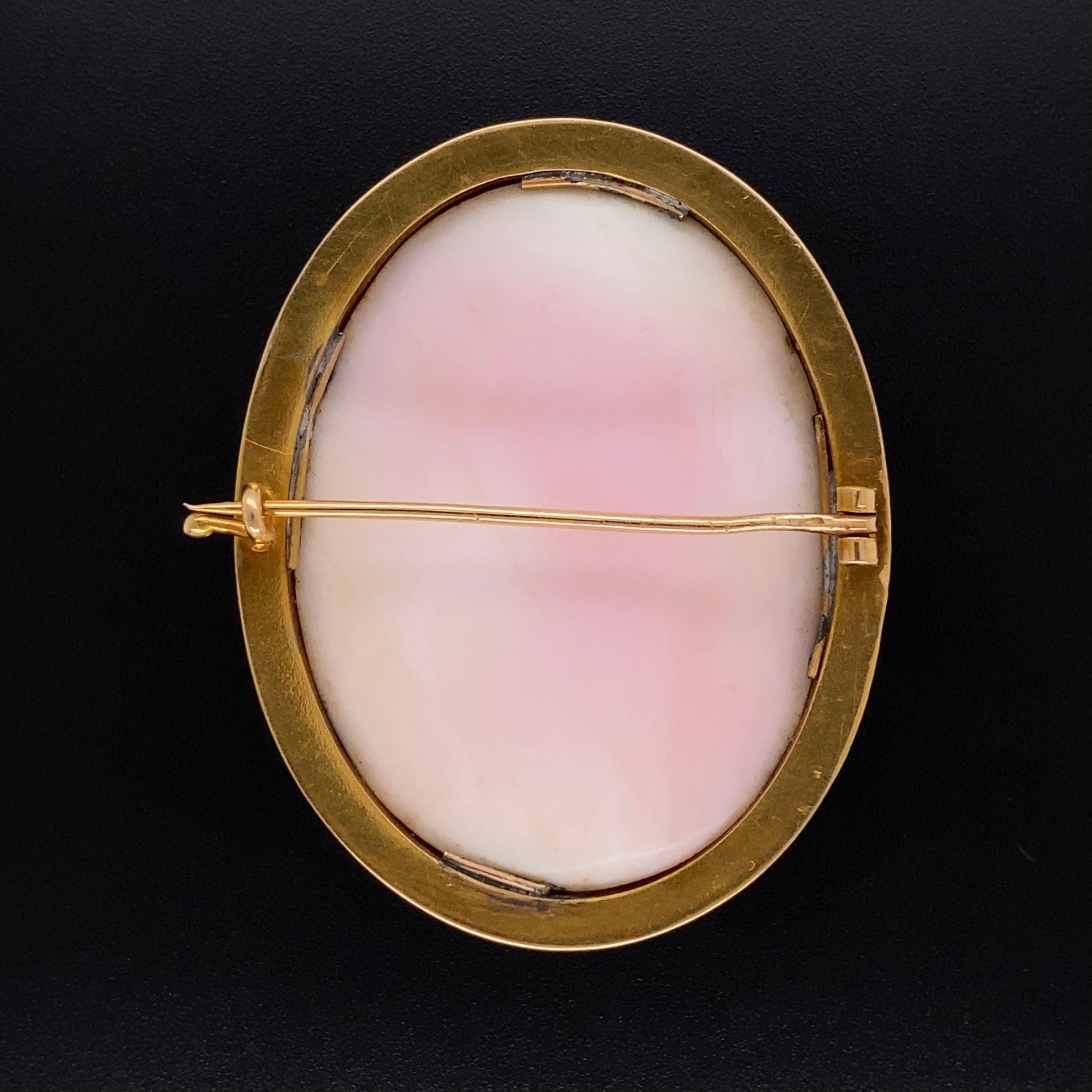 Beautiful Pink Coral Cameo Pin depicting a Beautiful Young Woman posing a striking a Romantic pose. The Hand carved oval Cameo is framed in a handmade 18K bezel engraved surround. Marked: 750 I. SAHA. Measuring approx. 1.32”w x 1.75”h x 0.36”d.