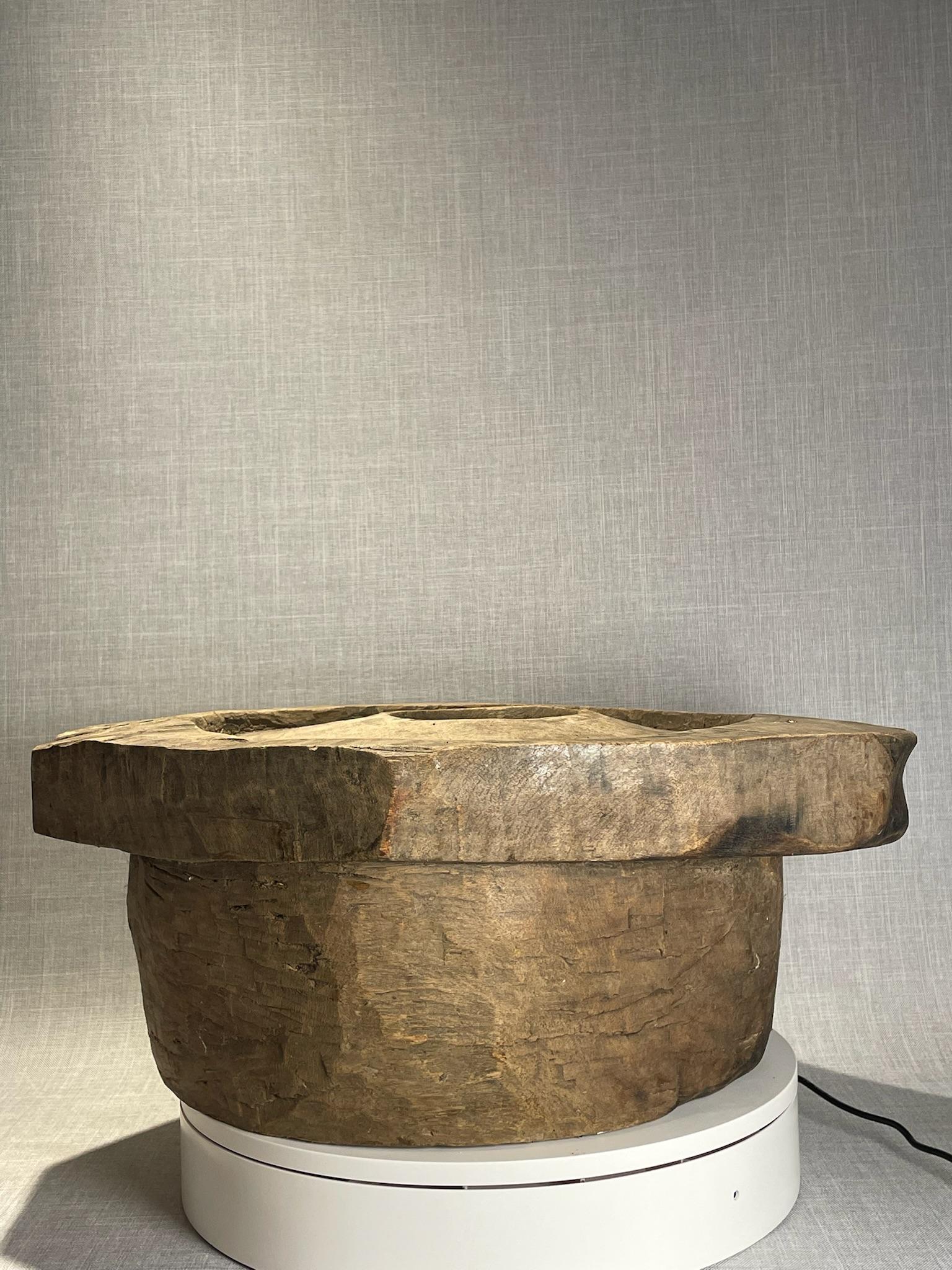 This antique hand-carved wooden piece is a remarkable example of rustic craftsmanship and utilitarian design. Most likely used as a mortar base or working tool in a traditional household, it carries the character of generations who relied on simple,