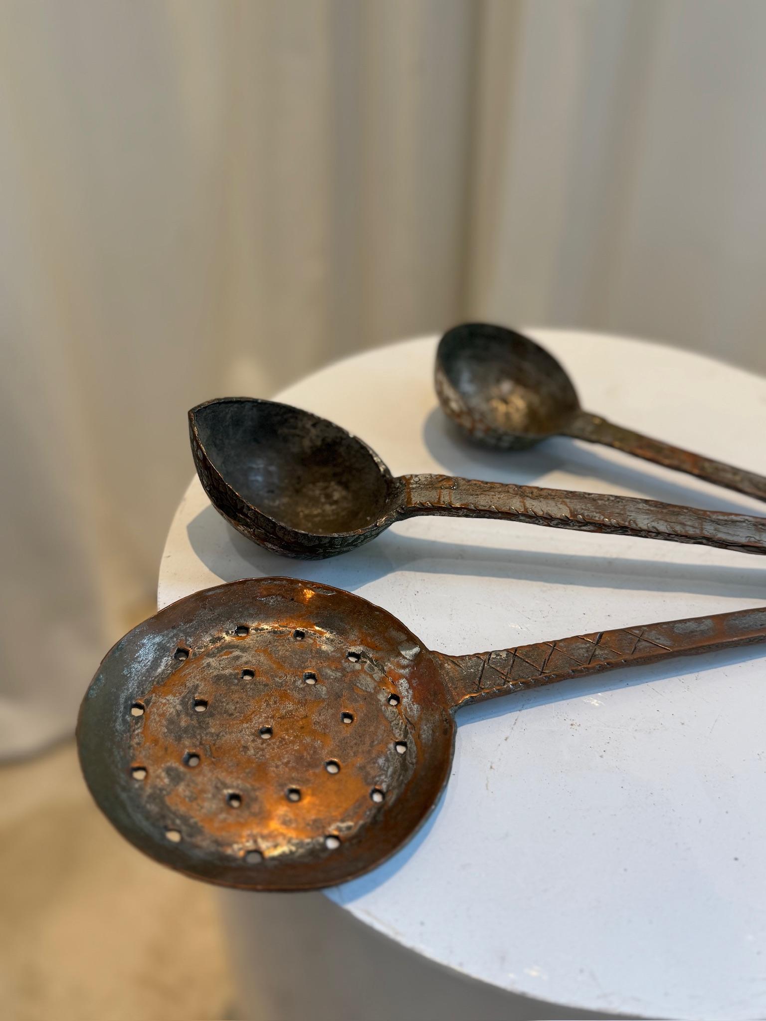A stunning set of three antique hand-forged iron cooking ladles, each with a unique rustic charm. These vintage kitchen utensils were crafted using traditional blacksmithing techniques, featuring long, sturdy handles and beautifully aged patina. The