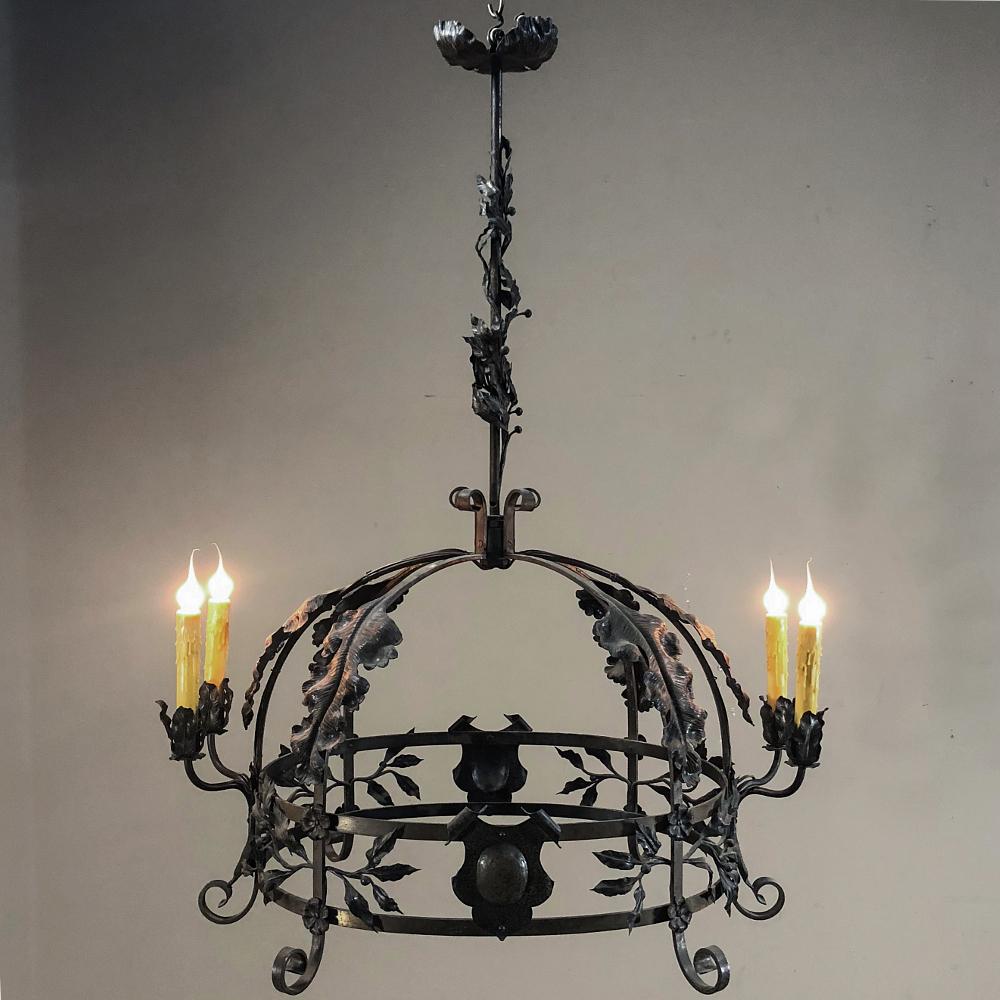 Antique Italian wrought iron chandelier features an intriguing dome shape with heraldic crests, lavish foliates, and four scrolled arms with intricately detailed embellishments. The crown shaped body connects to a shaft that leads up to the