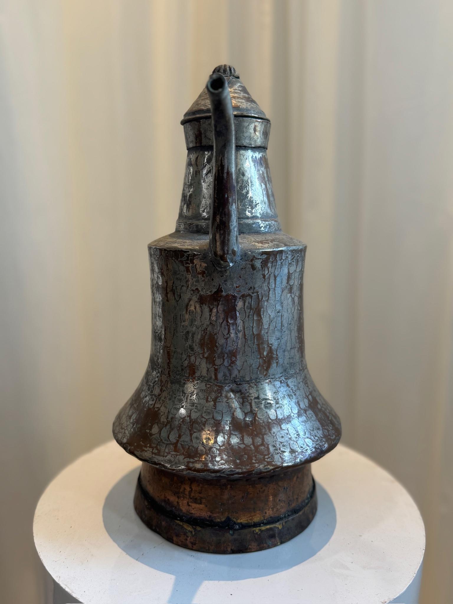 Cette exquise cafetière antique Dallah est un exemple étonnant de l'artisanat du Moyen-Orient. Martelée à la main à partir de métaux mixtes, probablement un mélange de cuivre et d'étain, cette pièce présente un bec élégamment incurvé et une poignée