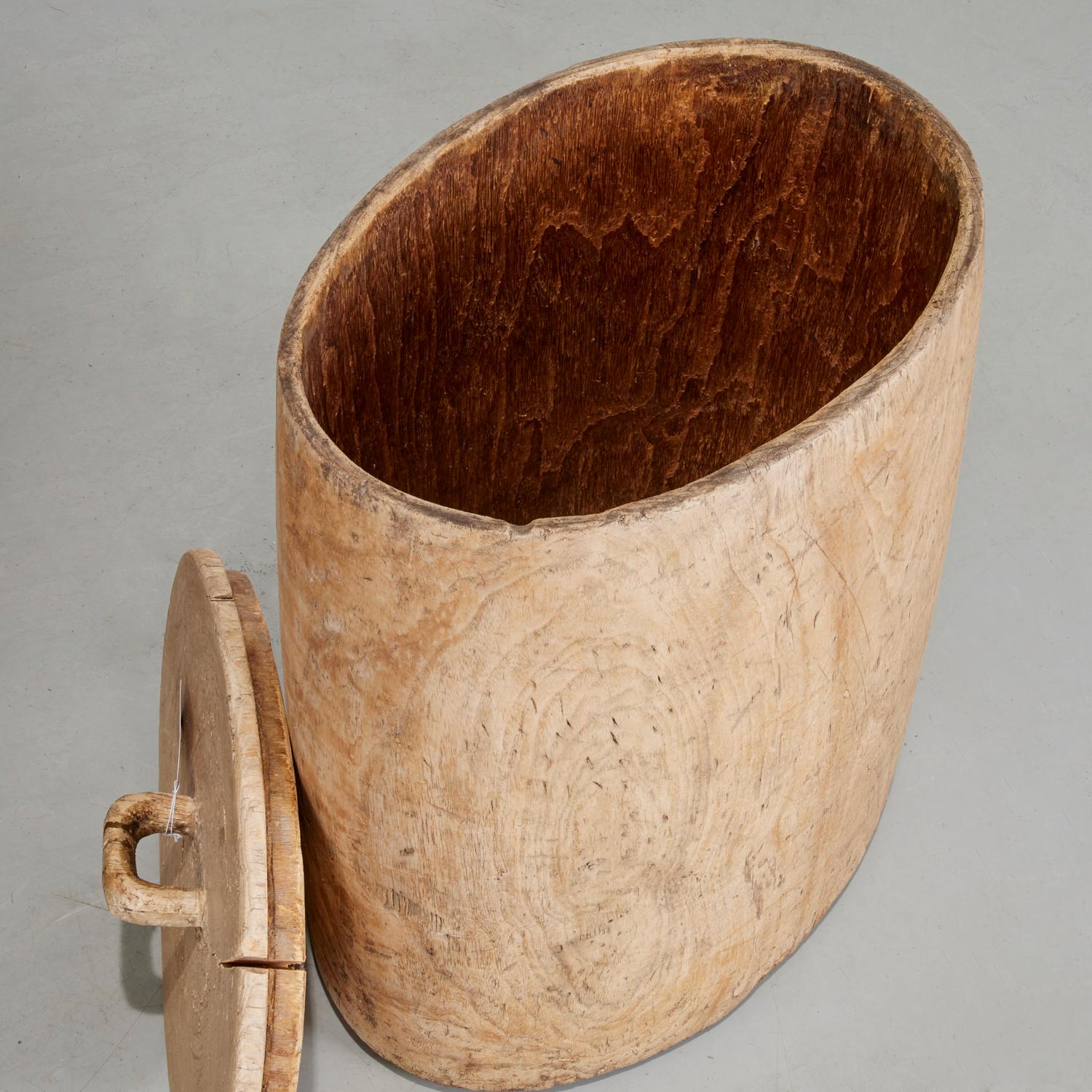 19th Century oval shaped lidded wooden rice container, likely Chinese. This is a hand hewn item made from a tree trunk and fitted with a base and lid made from the same wood. The lid is tight fitting and the handle shows evidence of long and