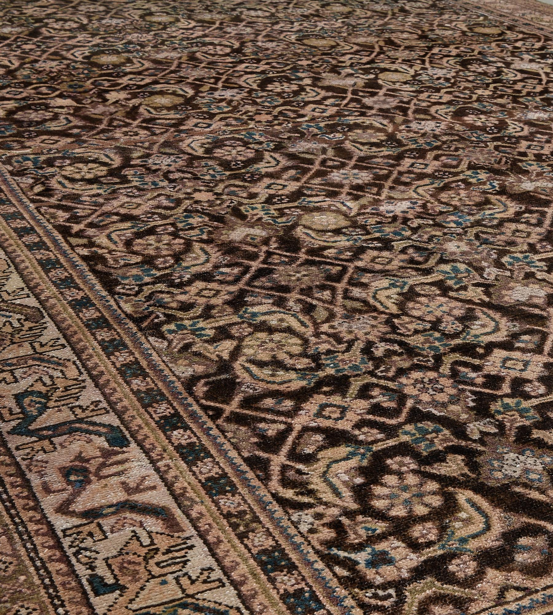 This antique Malayer rug has a chocolate-brown field with an overall herati-pattern design of ivory, sandy-yellow and hints of sea-blue, in an ivory border of fox-brown and sandy-yellow angular floral vine between chocolate-brown and