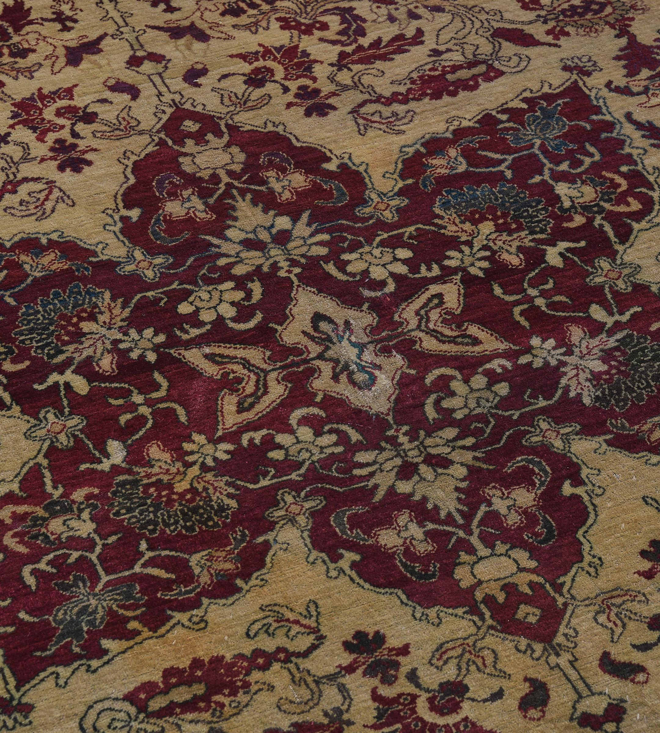 This antique, circa 1910, Indian Agra rug has a sandy-yellow field with a delicate burgundy-red and shaded green floral and leafy vine around a large central burgundy-red cusped medallion containing palmette and floral vine with palmette pendants,