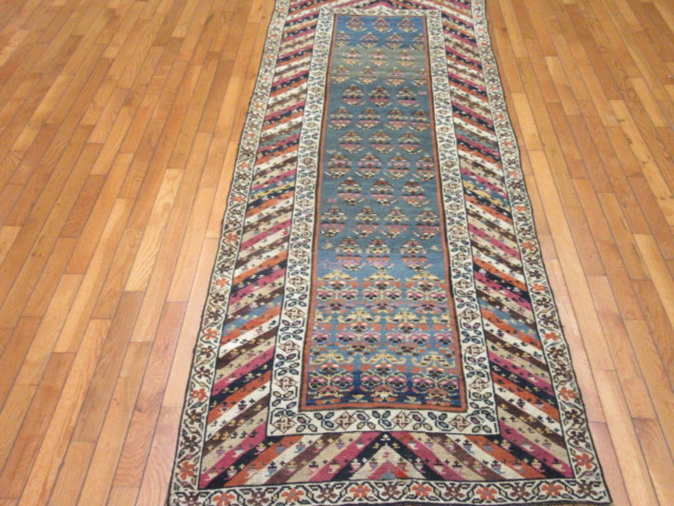 This is an antique hand-knotted rugs from the village Genjeh in the Caucuses. It is made with all wool colored with natural dyes in a traditional paisley design on a light blue field and frames with the slanted trade mark design of the Genjeh rugs.