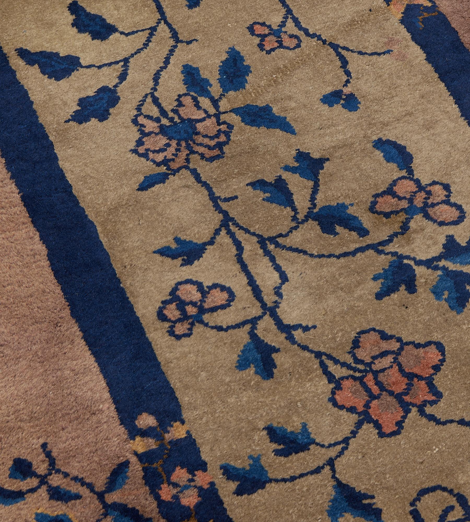 Esta alfombra china antigua, de hacia 1920, tiene un campo marrón topo sombreado con una delicada enredadera de hojas añil y azul claro que emite cabezas de flores rosa empolvado, en un amplio borde rosa empolvado de jarrones en flor y tallos de