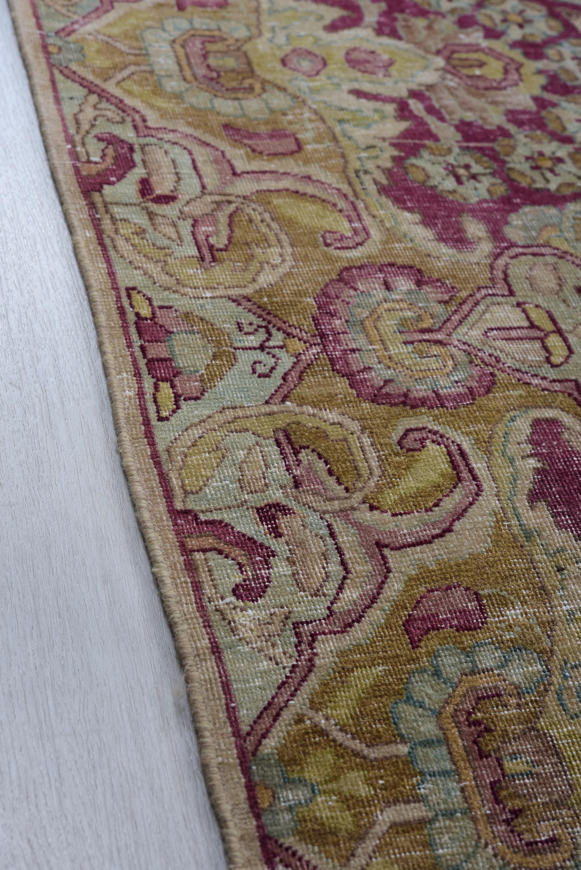 This antique Kerman rug showcases an intricate Persian floral design, featuring a gracefully woven central medallion and scrolling arabesques in a rich blush, taupe, and deep burgundy palette. The detailed blossoming vines, palmettes, and curved