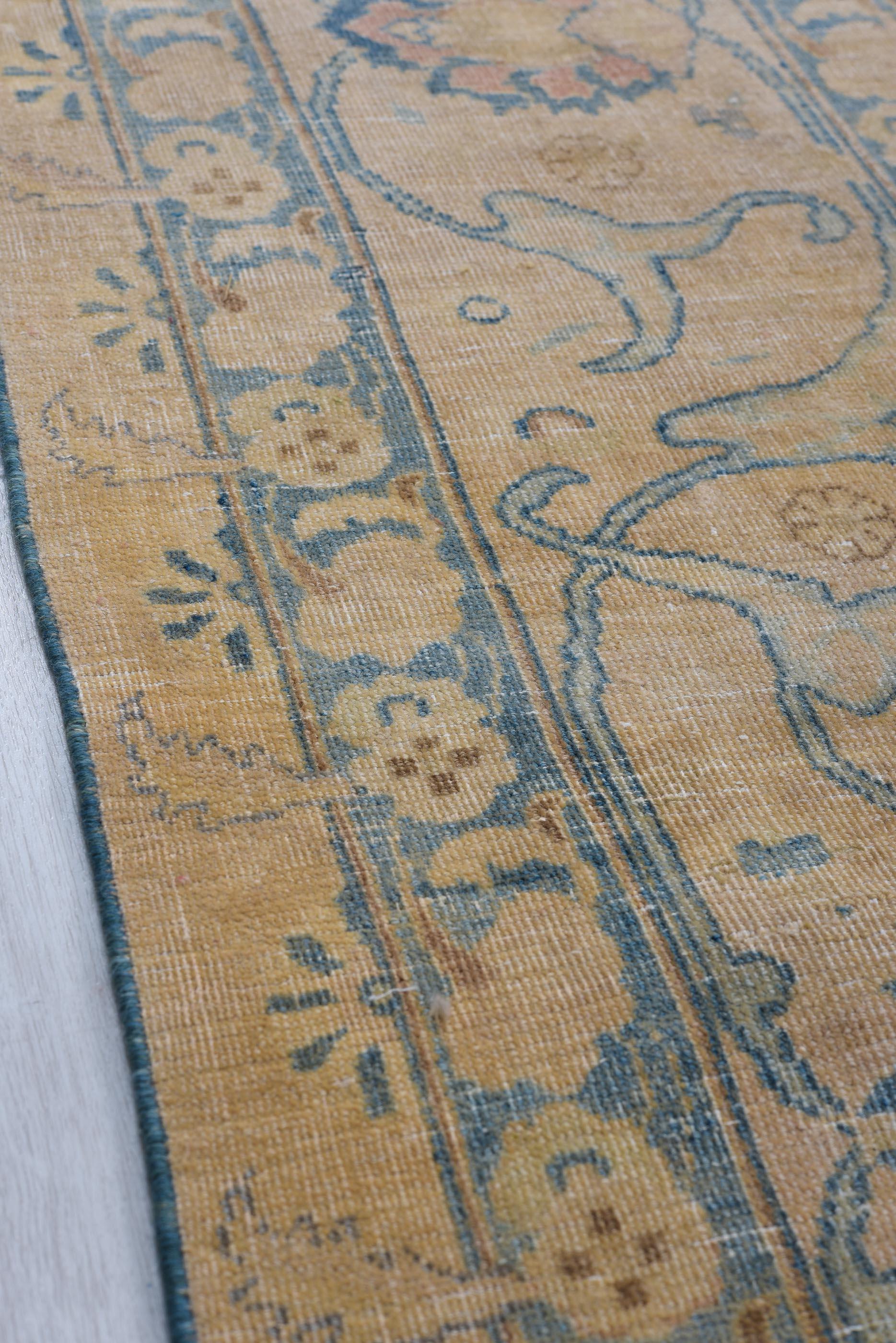Dieser antike Mesh-Teppich zeigt ein wunderschön gealtertes botanisches Muster, gewebt in einer warmen, erdigen Farbpalette aus Hellbraun, gedämpftem Gold und sanftem Blau. Das zentrale Feld ist mit zarten floralen Motiven und geometrischen Rosetten