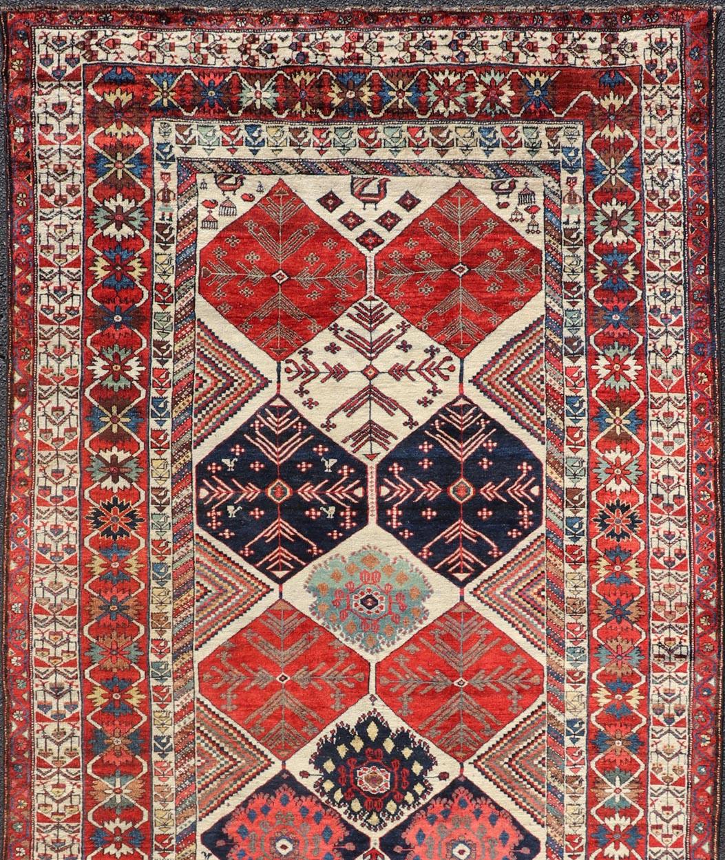 This antique Persian Bakhtiari rug has been hand-knotted in wool and features an all-over sub-geometric diamond design rendered in multicolor, set upon an ivory background. A complementary, multi-tiered border encompasses the entirety of the piece;