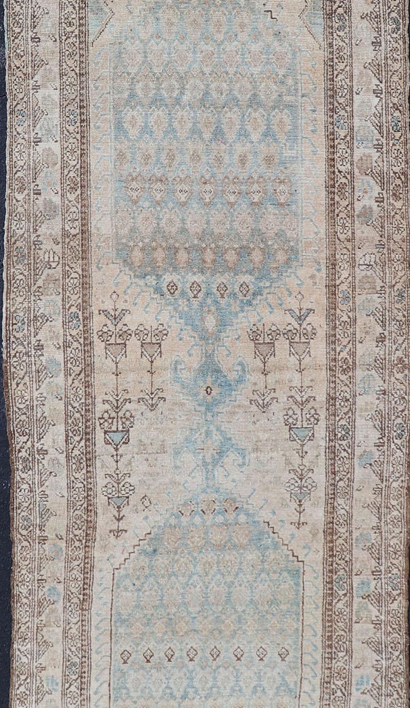 This antique hand-knotted Persian Malayer runner features a large sub-geometric double medallion design, enclosed within a complementary multi-tiered border. The rug is rendered in blue, brown, ivory and cream tones; making this rug a superb fit for