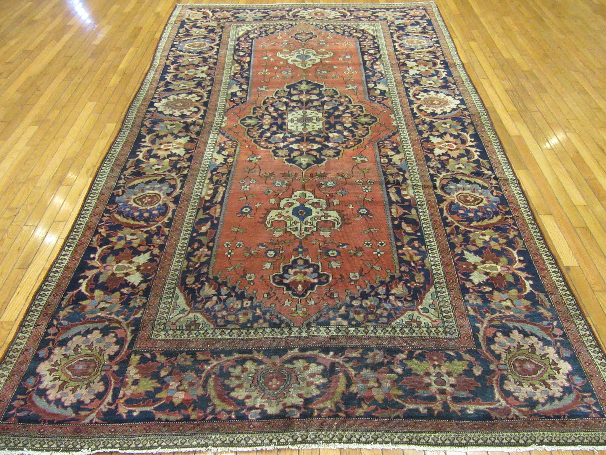 This is an antique hand knotted Persian Sarouk Farahan rug with a Classic traditional central medallion design on a brick red color field and a wide navy border. The rug has a hard to find size of 6' 3” x 10' 8” a perfect rug for a foyer or anywhere