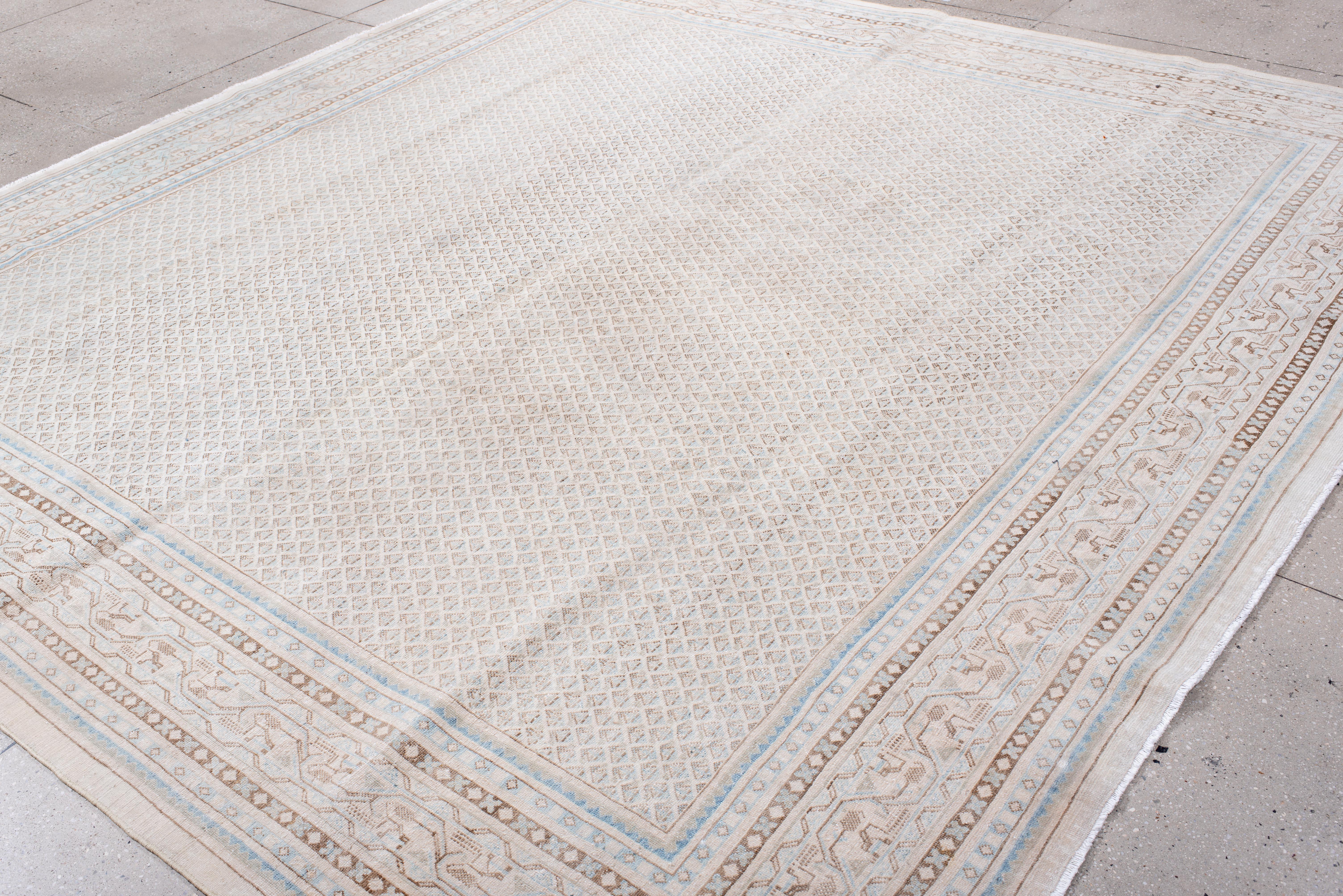 This antique Saraband rug showcases a delicate and refined geometric lattice pattern, woven in soft ivory, beige, and hints of pale blue. The intricate repeating boteh motifs within the field lend a sense of structure and depth, while the