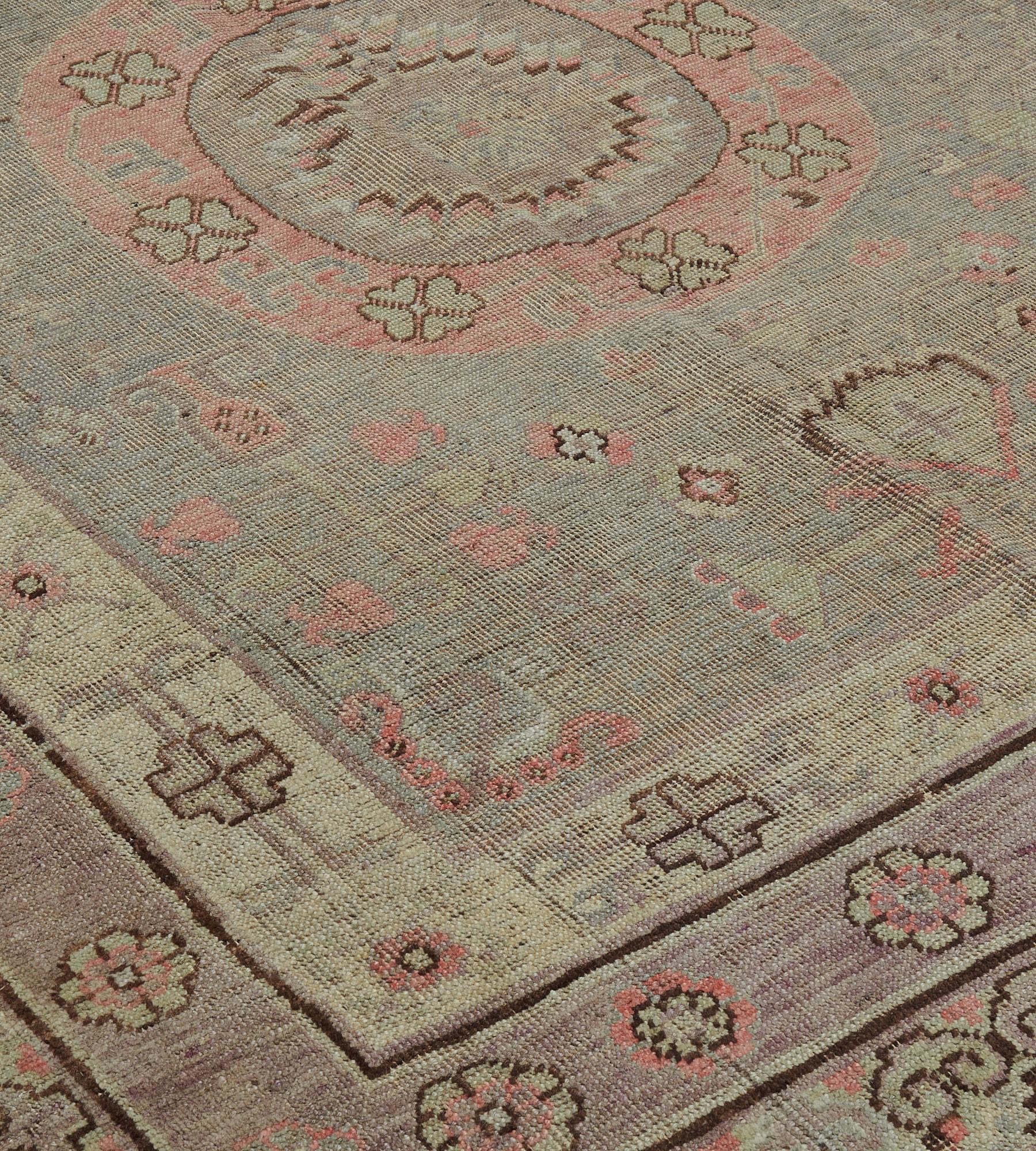 This antique Khotan rug features a shaded steel-blue field with a variety of floral motifs around a pair of dusty-pink roundels each with a band of linked flowerheads around a shaded steel-blue central panel with a radiating flowerhead, in a shaded