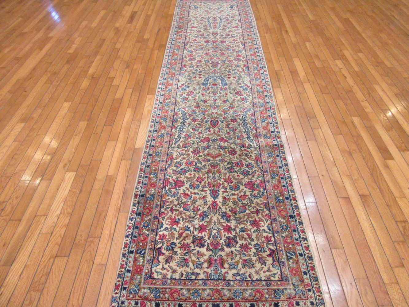 This is an antique hand knotted Persian Kerman runner rug. It has a traditional small scale floral pattern in primary colors on an ivory color background. The rug is made with wool on a cotton foundation. It measures 2' 10'' x 11' 5''.