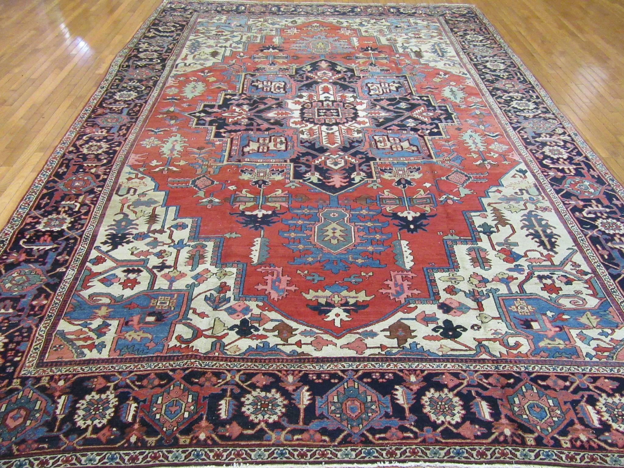 This is a genuine antique room size hand-knotted Persian Serapi rug. It is made with fine wool colored with natural dyes on a cotton foundation. It has the central and corner medallion geometric design trademark of these type of rugs. The rug
