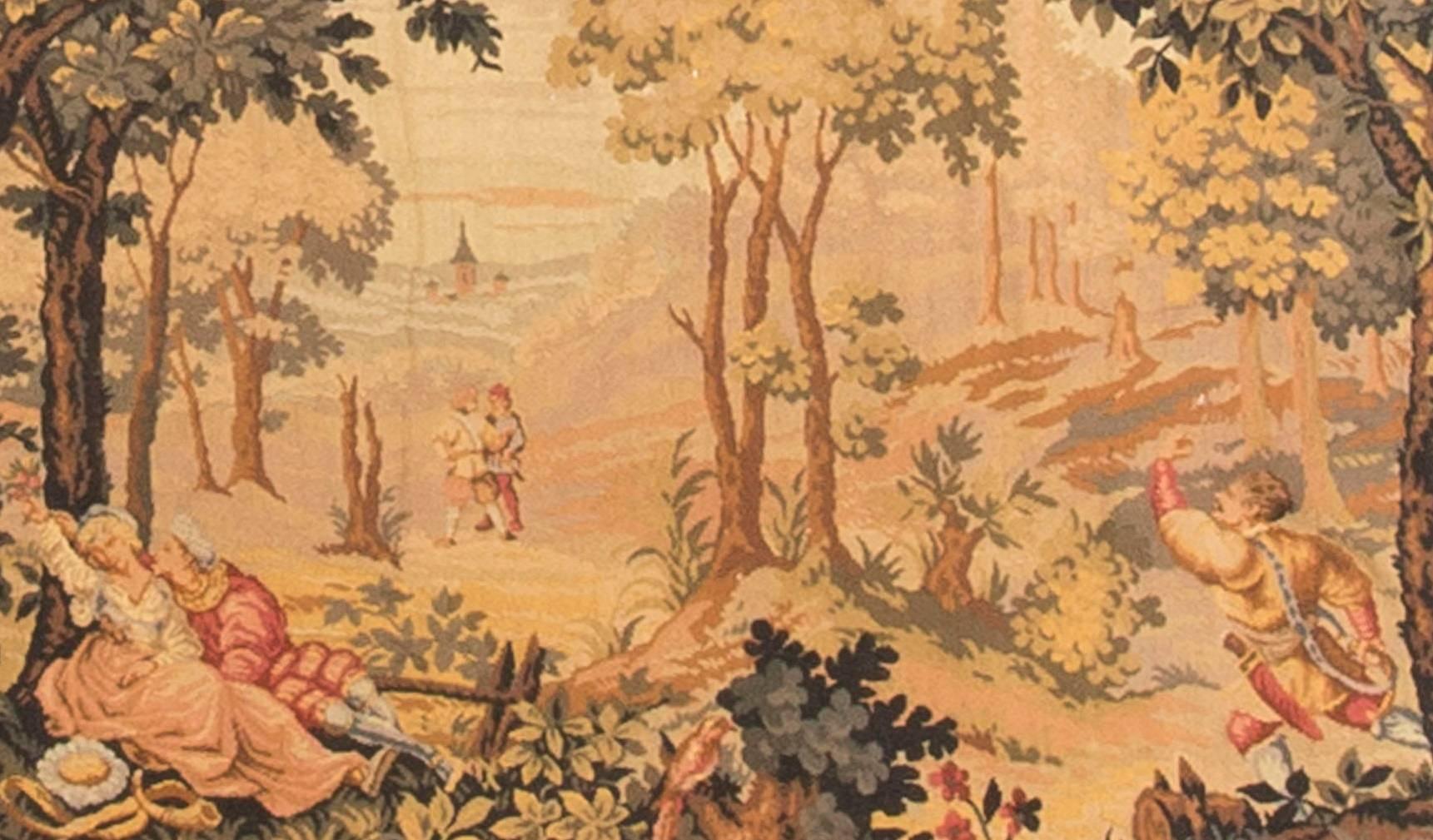 A hand-loomed French tapestry, circa 1890. Depicting a pair of lovers in the foreground and to their side a huntsman rushing to join his friends. The country scene is enclosed a in a floral border.
 