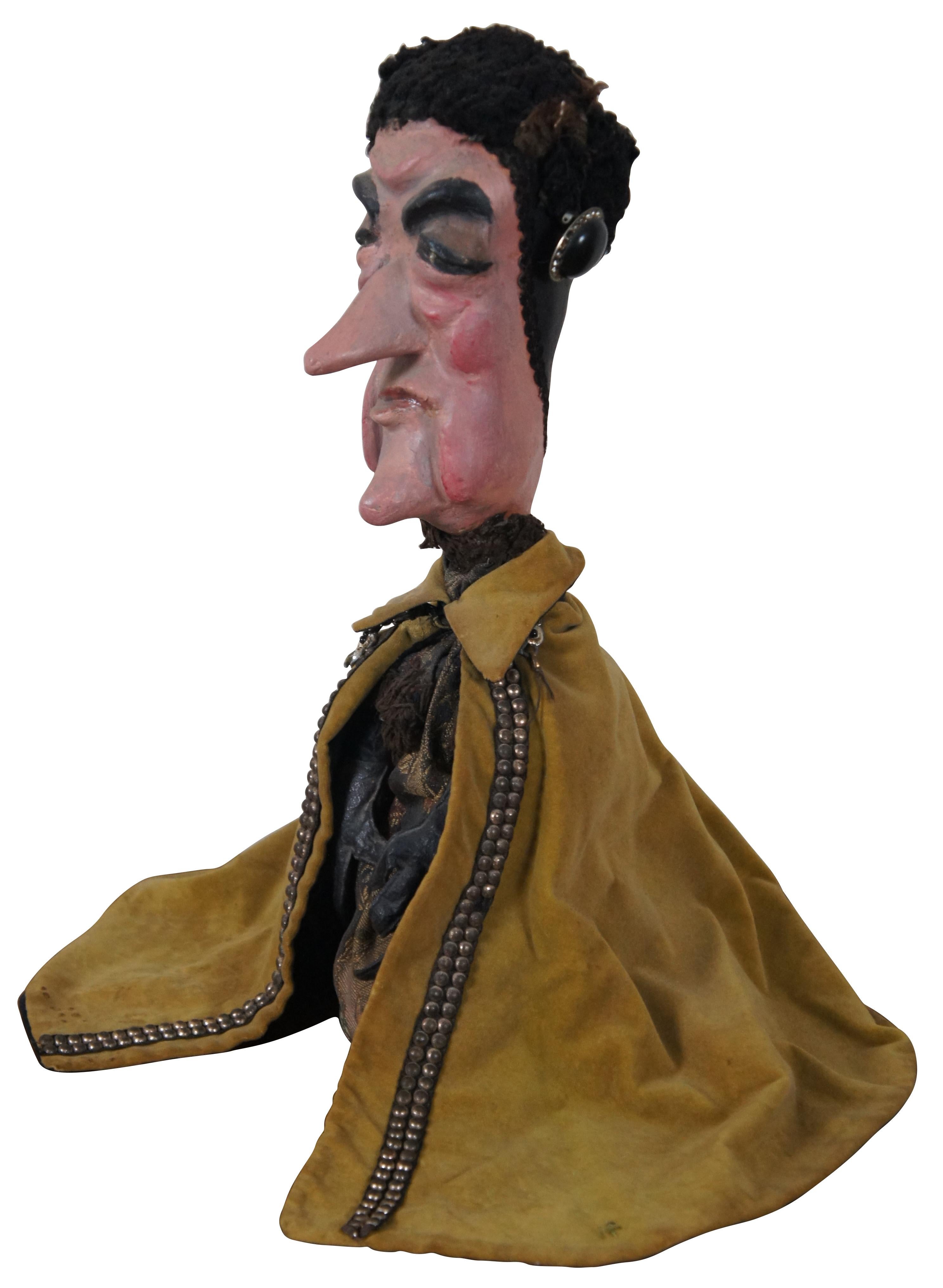 Antique hand made and painted paper mache hand puppet in the shape of a masculine human figure wearing a fur cap, brocade tunic, leather gloves and a mustard yellow velvet cape. Comes with a vintage distressed painted stand.