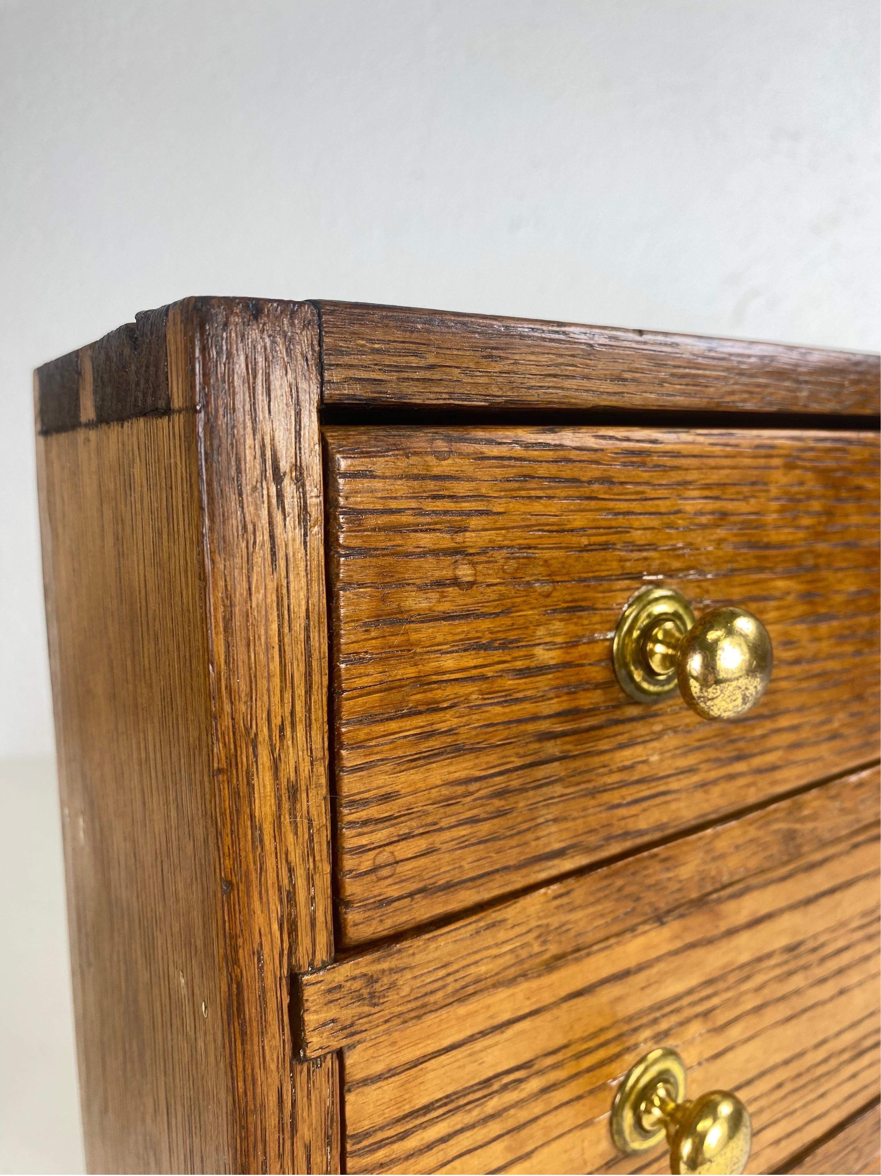 This is an antique handmade solid oak miniature Chester drawers. This dresser top chest of drawers has its original solid brass hardware. This handmade piece has dovetailing at the top of the chest, as well as the interior of the drawers. This piece
