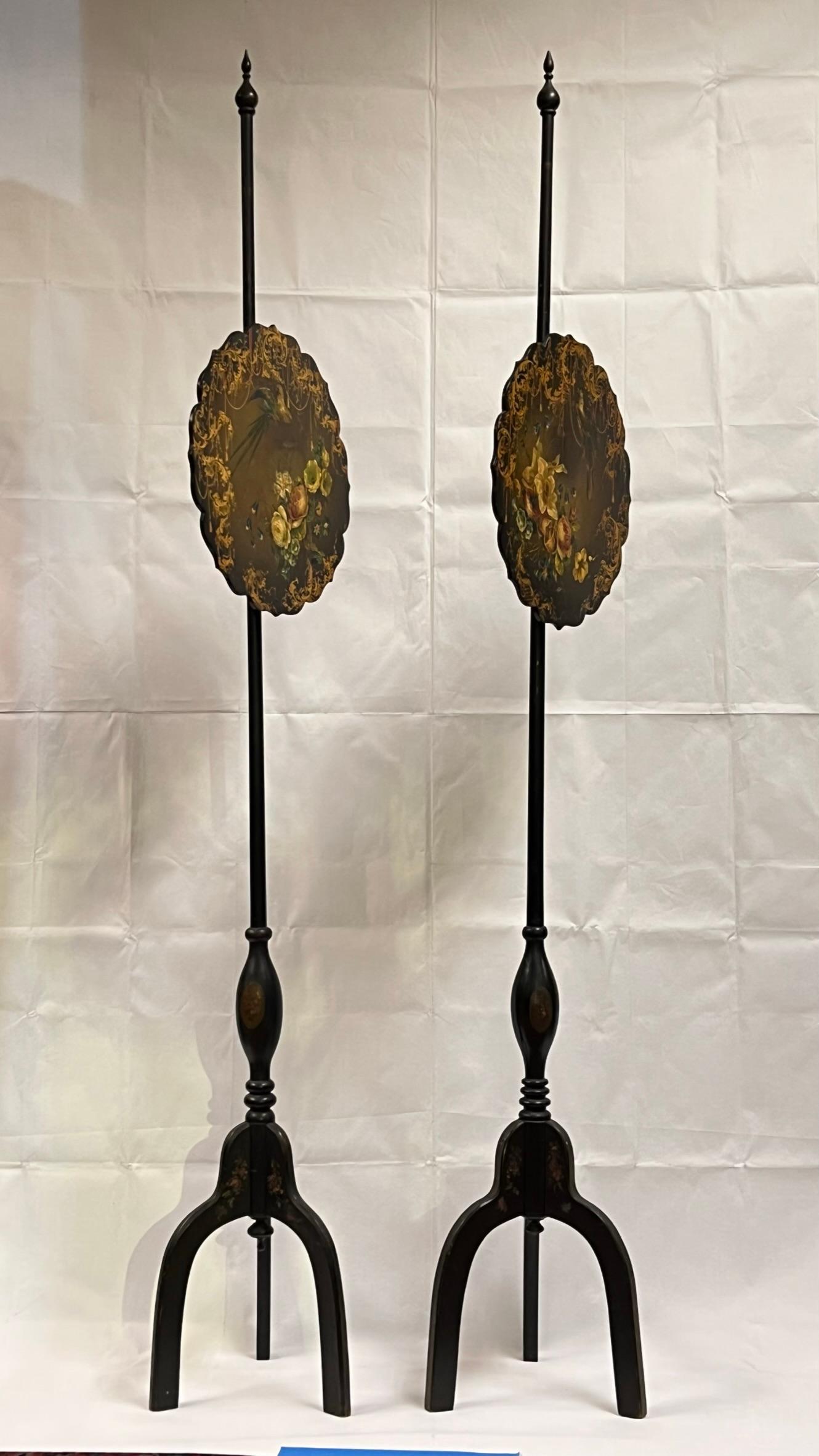 Pair of ebonized pole screens with fine floral painted finishes on tripod legs.