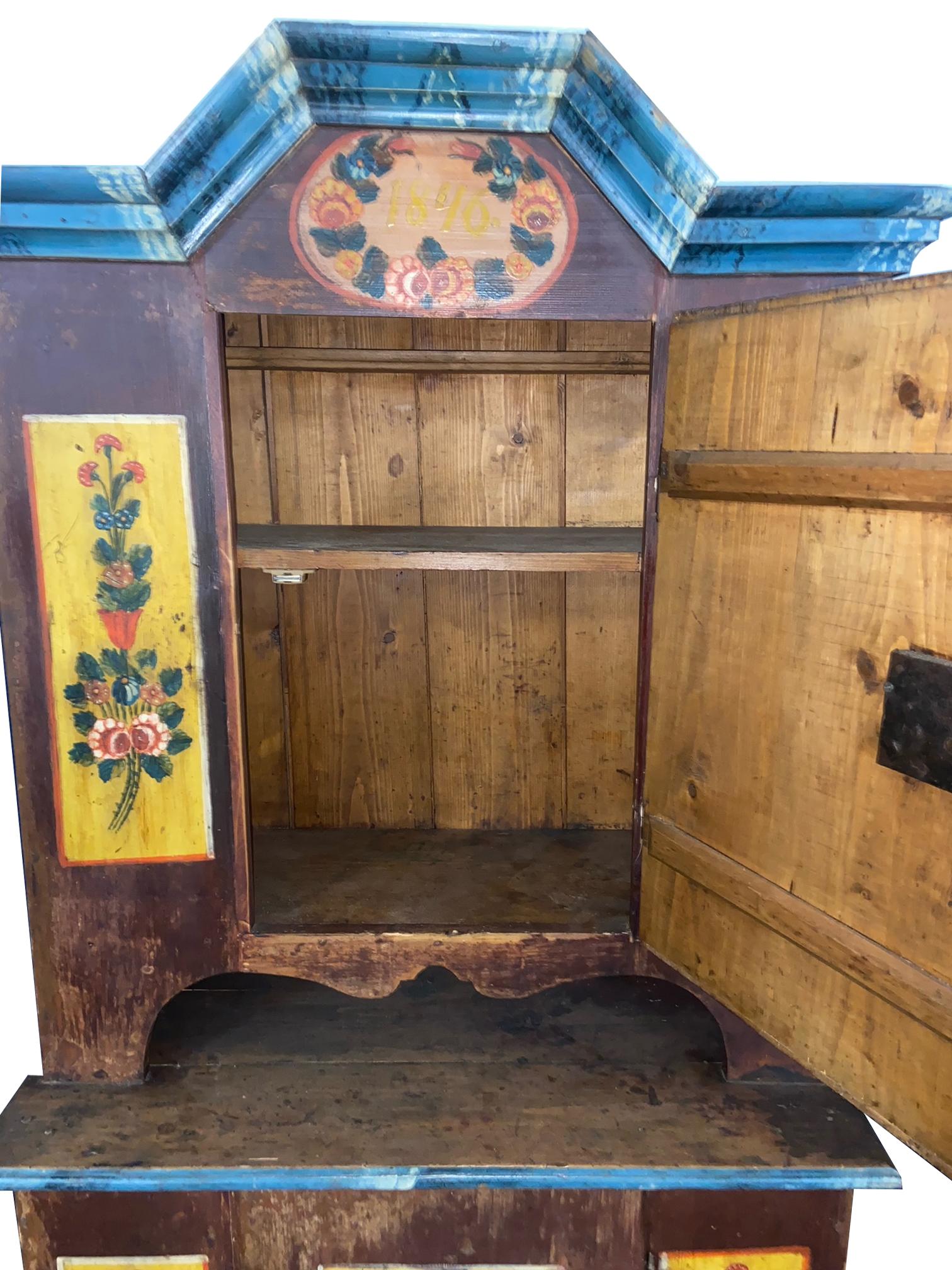 This burgundy cupboard features beautiful original hand-painted decorations throughout. Yellow panels portraying vases full of flowers adorn the doors and a blue painted cornice meant to resemble marble adorns the top.

Circa