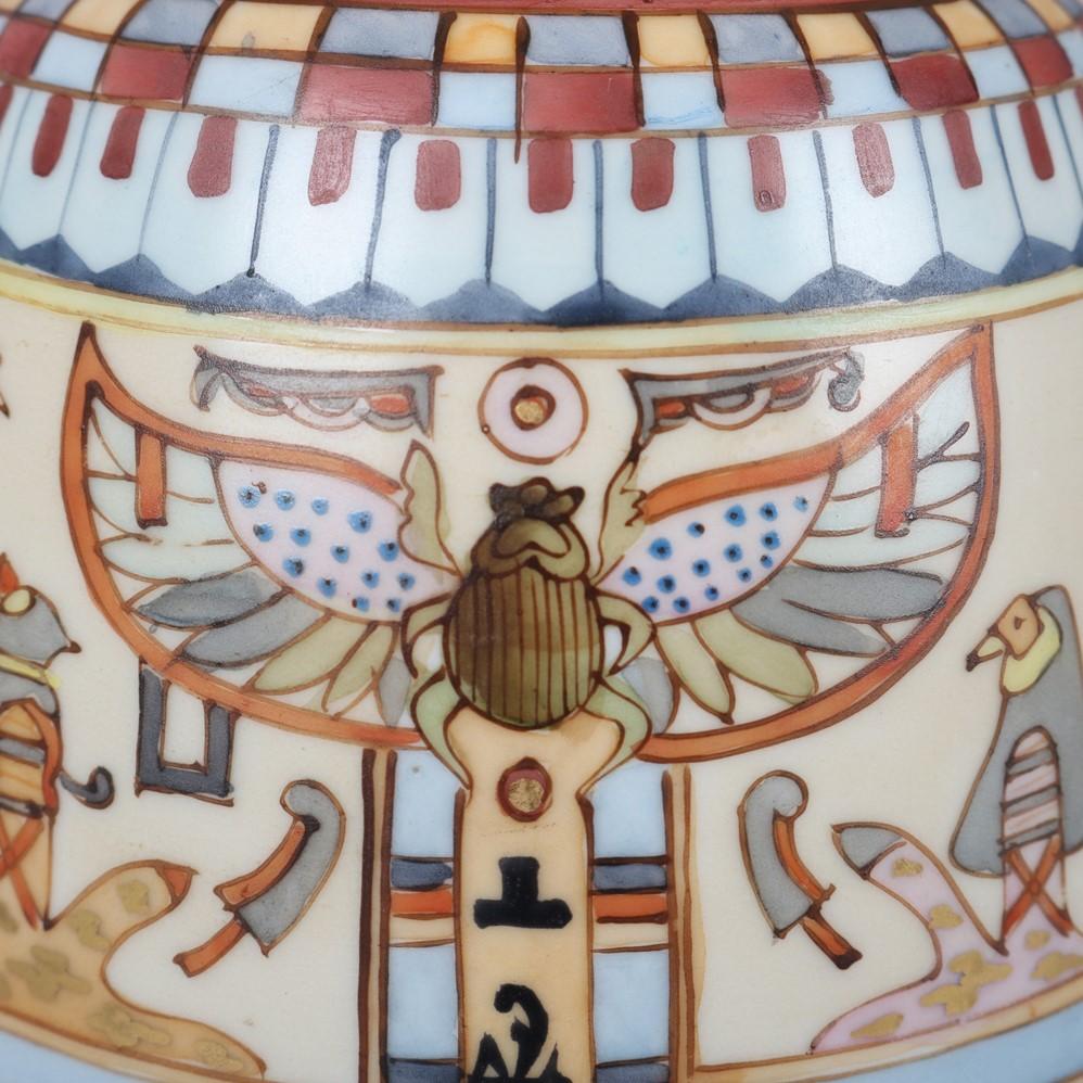 An antique Japanese Nippon Egyptian Revival vase offers porcelain construction with hand painted and gilt allover design including figures and ceremonial elements, seated on geometric form feet, circa 1920.

Measures: 8.25