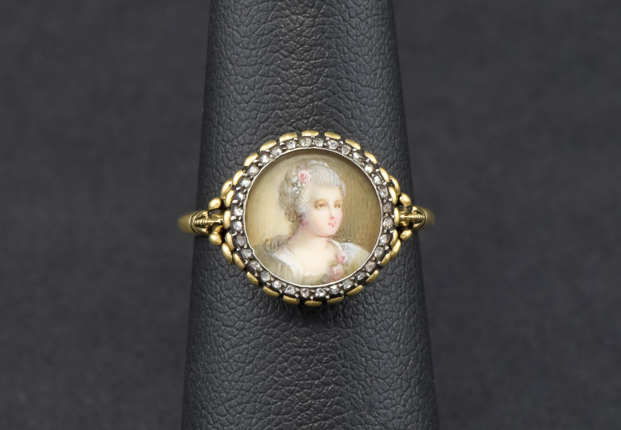 Dieser besondere Ring ist ein Unikat, das aus einer schönen antiken, handgemalten Porträt-Anstecknadel mit Diamanten gefertigt wurde.

Der aus 18-karätigem Gelbgold und Silber gefertigte Ring zeigt ein originales, handgemaltes Aquarellporträt einer